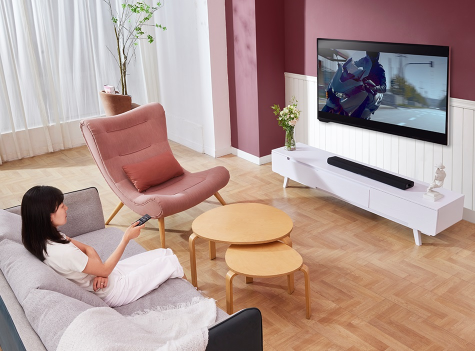 Kobieta ogląda telewizję w nowoczesnym salonie. Widoczne są TV, kanapa i stoliki kawowe.