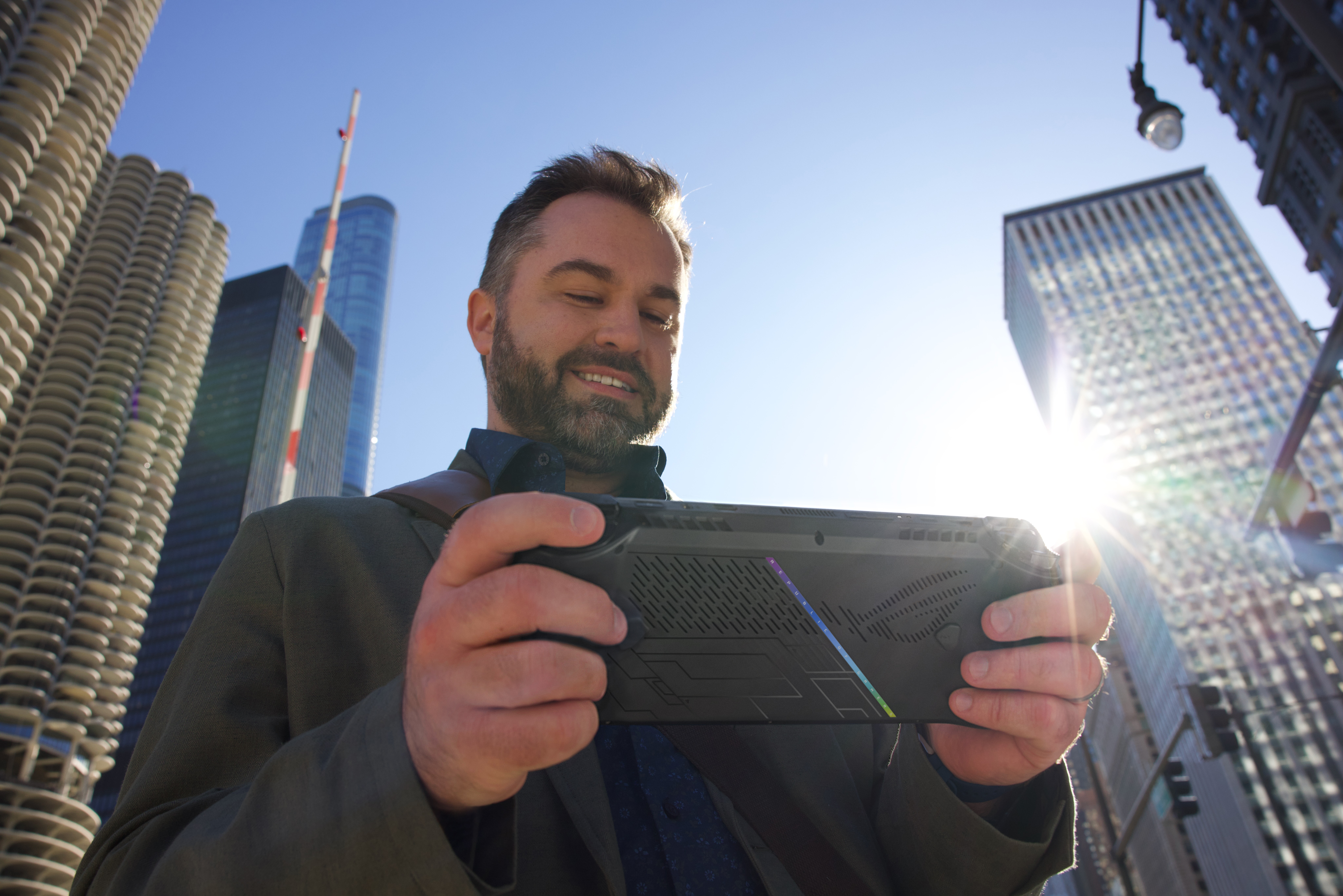 Ein Mann in einem Mantel hält ein Handheld-Spielgerät vor einer Stadtlandschaft.