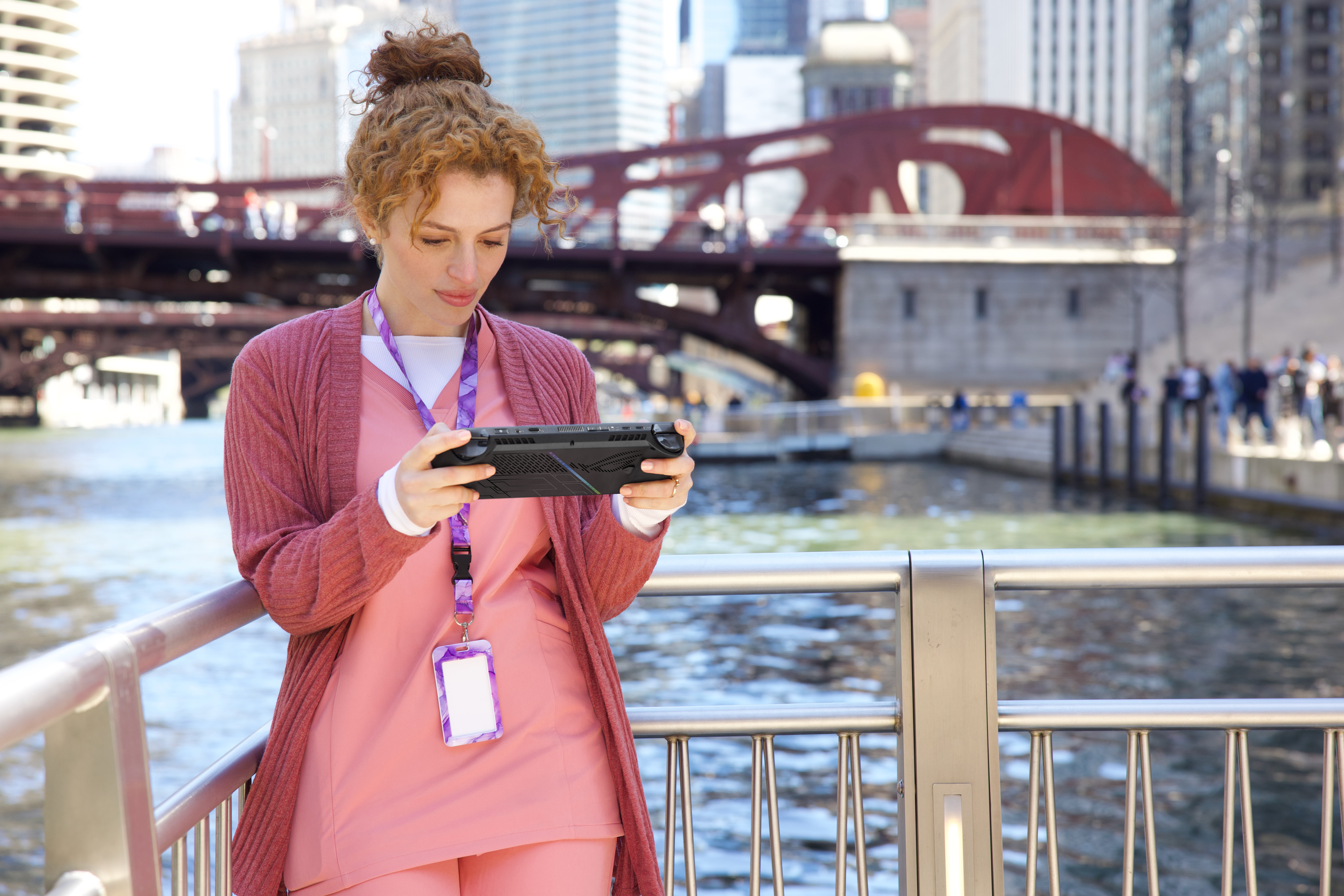Frau benutzt eine Handheld-Konsole an einem Fluss. Sie trägt ein rosa Outfit.