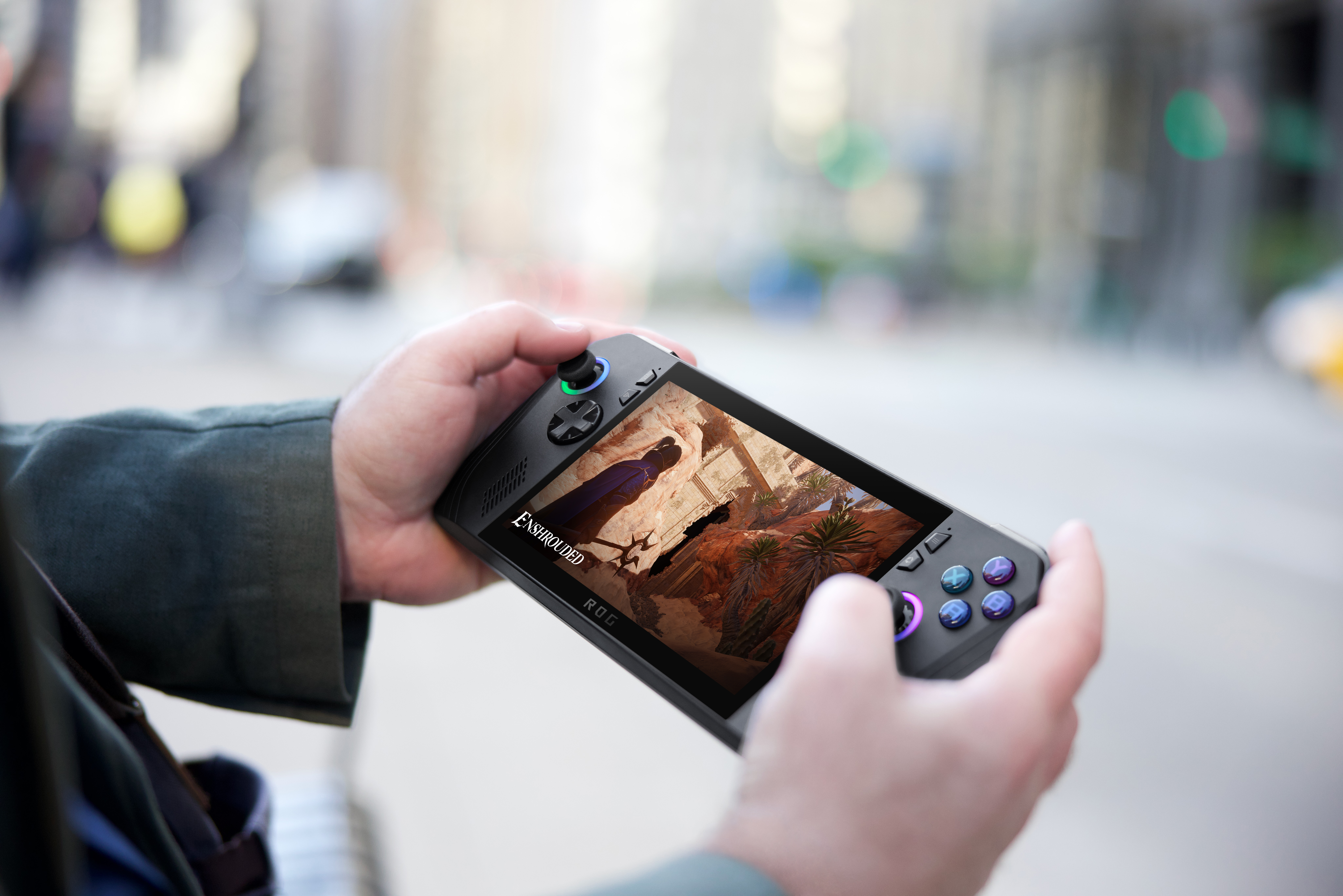 Hände halten ein Handheld-Gaming-Gerät, das eine Spielszene auf dem Bildschirm zeigt. Verschwommener Stadt-Hintergrund.