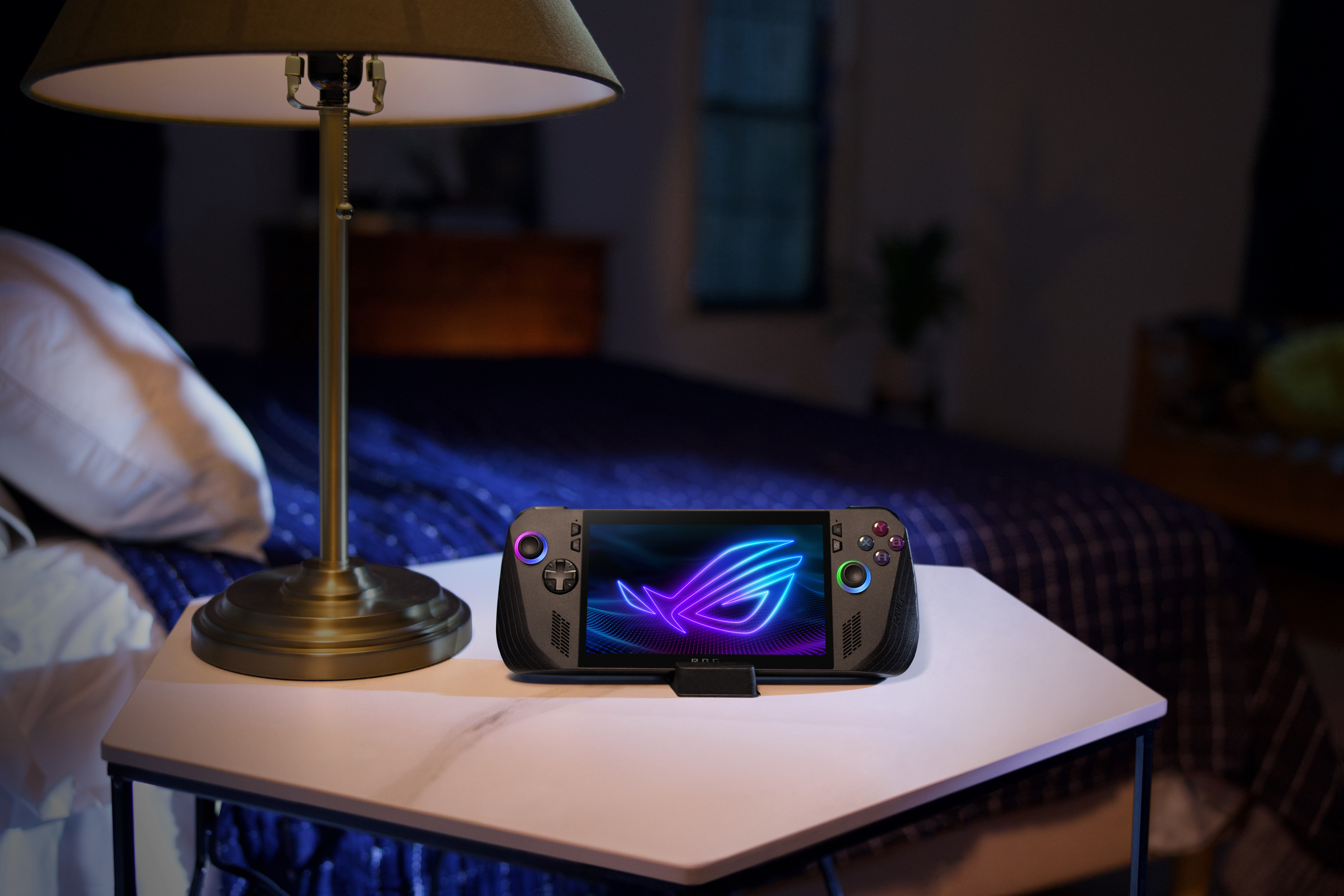 Dunkler Raum mit einem Gaming-Handheld und einer Lampe auf einem Tisch. Der Bildschirm zeigt ein Logo.