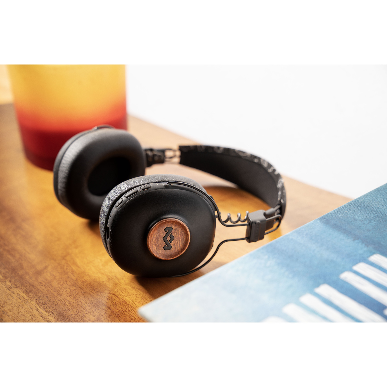Casque noir sur une table en bois à côté d'un livre bleu et d'une tasse jaune et rouge.
