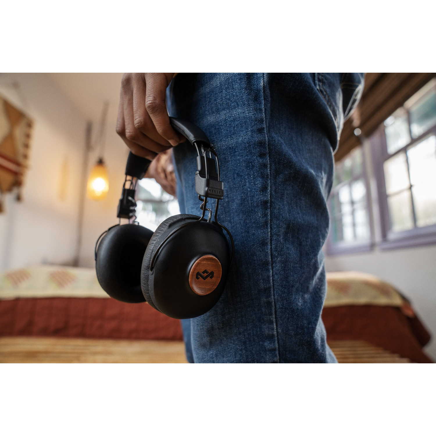 Personne tenant un casque noir avec détails en bois. Jean et une pièce en arrière-plan.