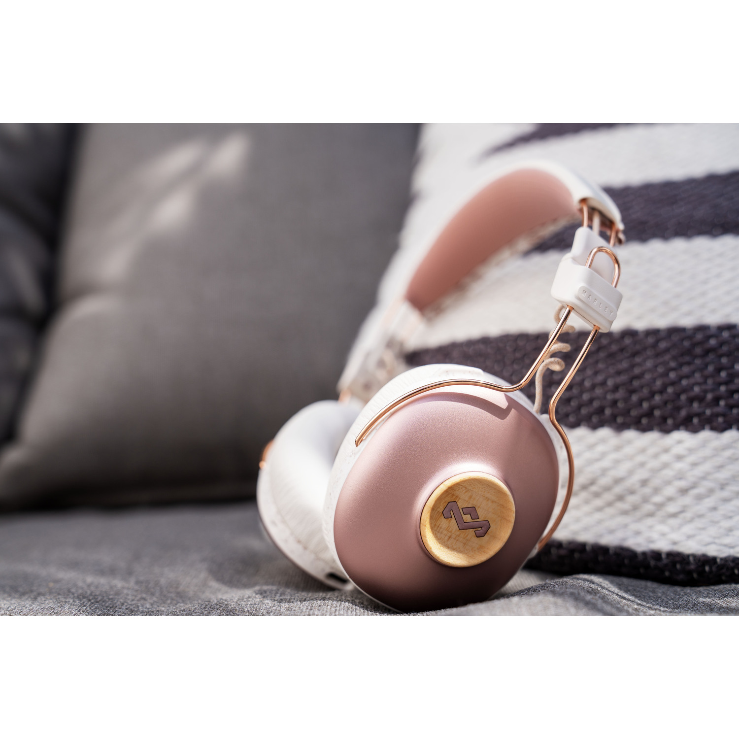 Casque rose doré et blanc posé sur un coussin gris, près d'un oreiller rayé.