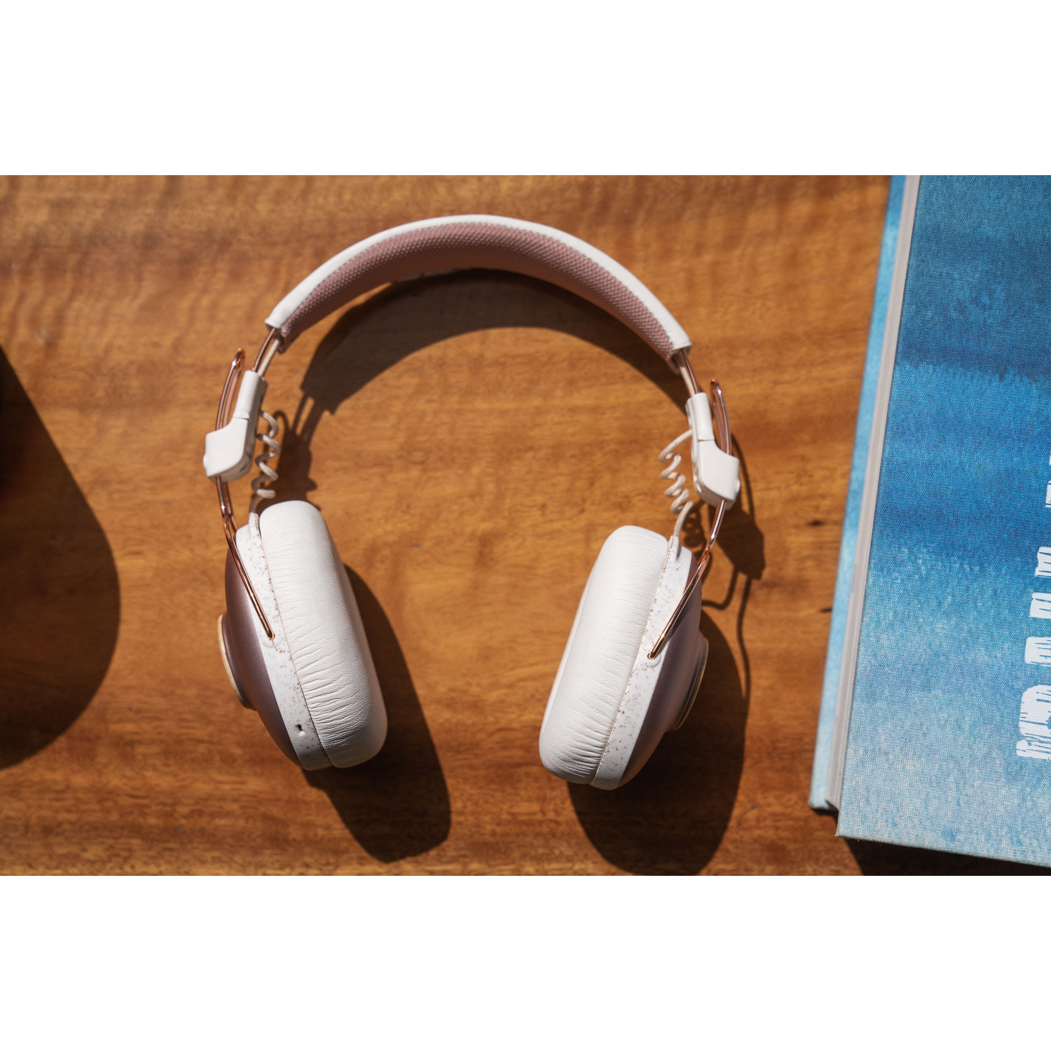 Casque rose doré et blanc sur une table en bois à côté d'un livre bleu.