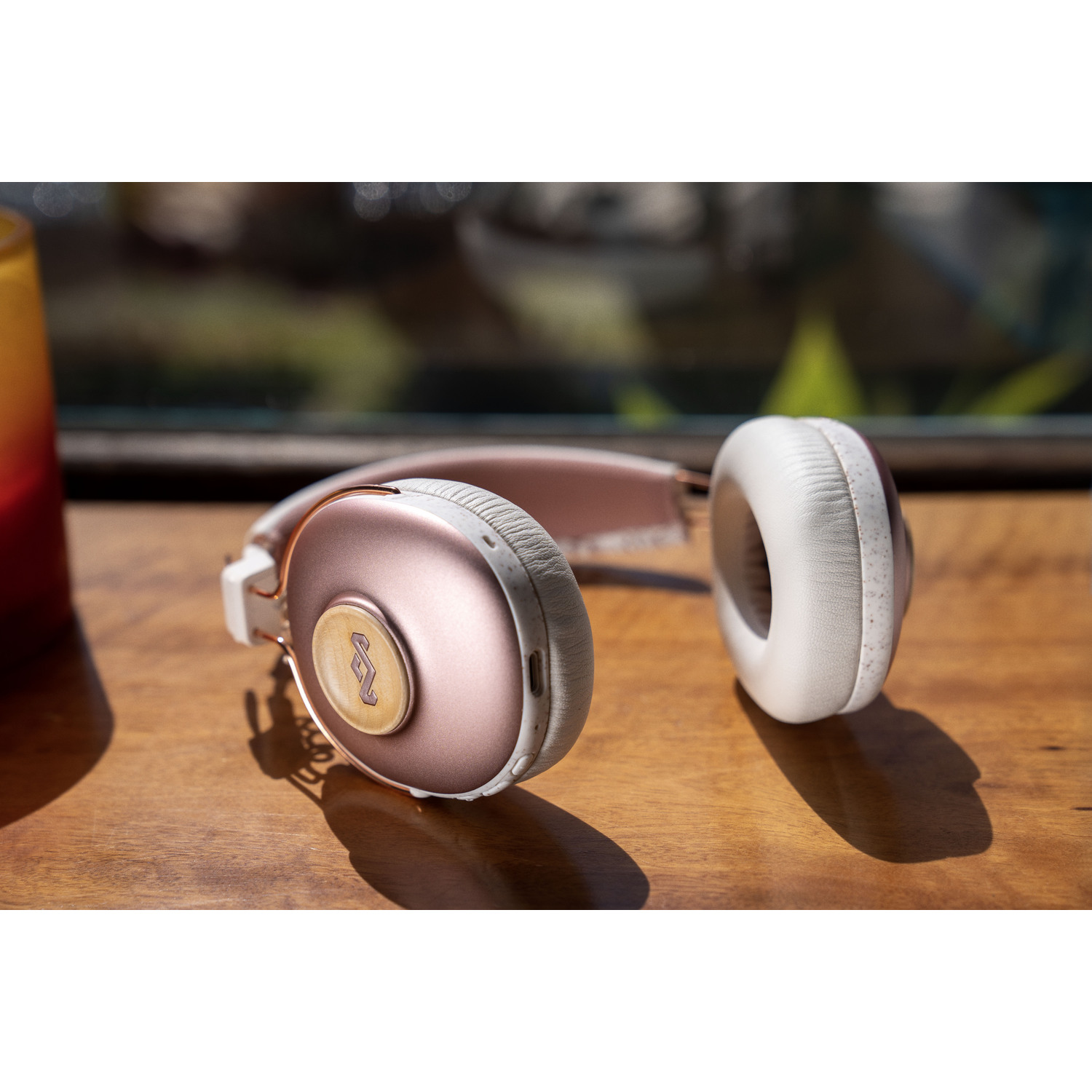 Un casque rose doré et blanc posé sur une table en bois. Les écouteurs sont visibles.