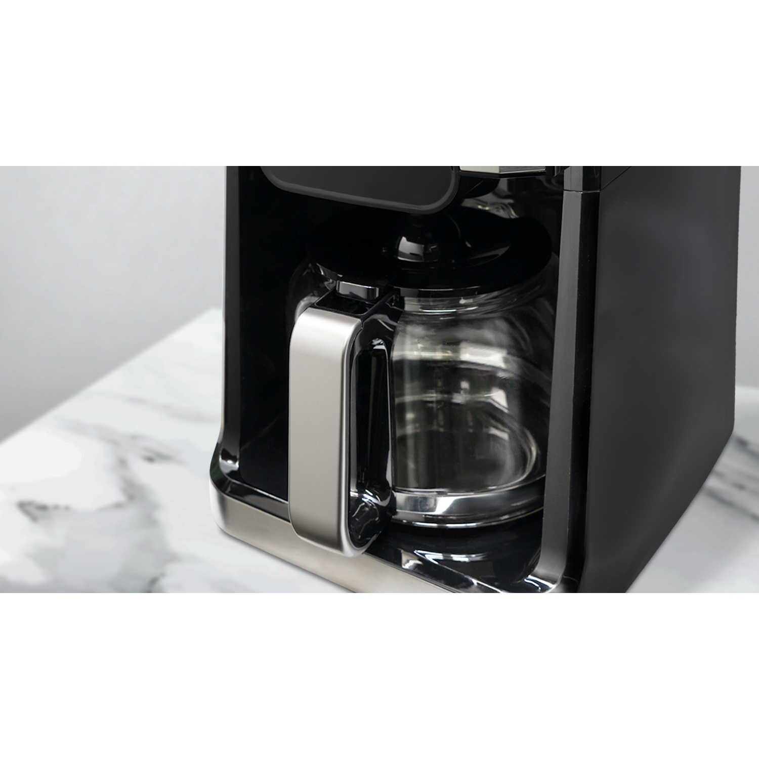 Caffettiera nera con caraffa in vetro, dettagli in acciaio inox e superficie in marmo bianco.