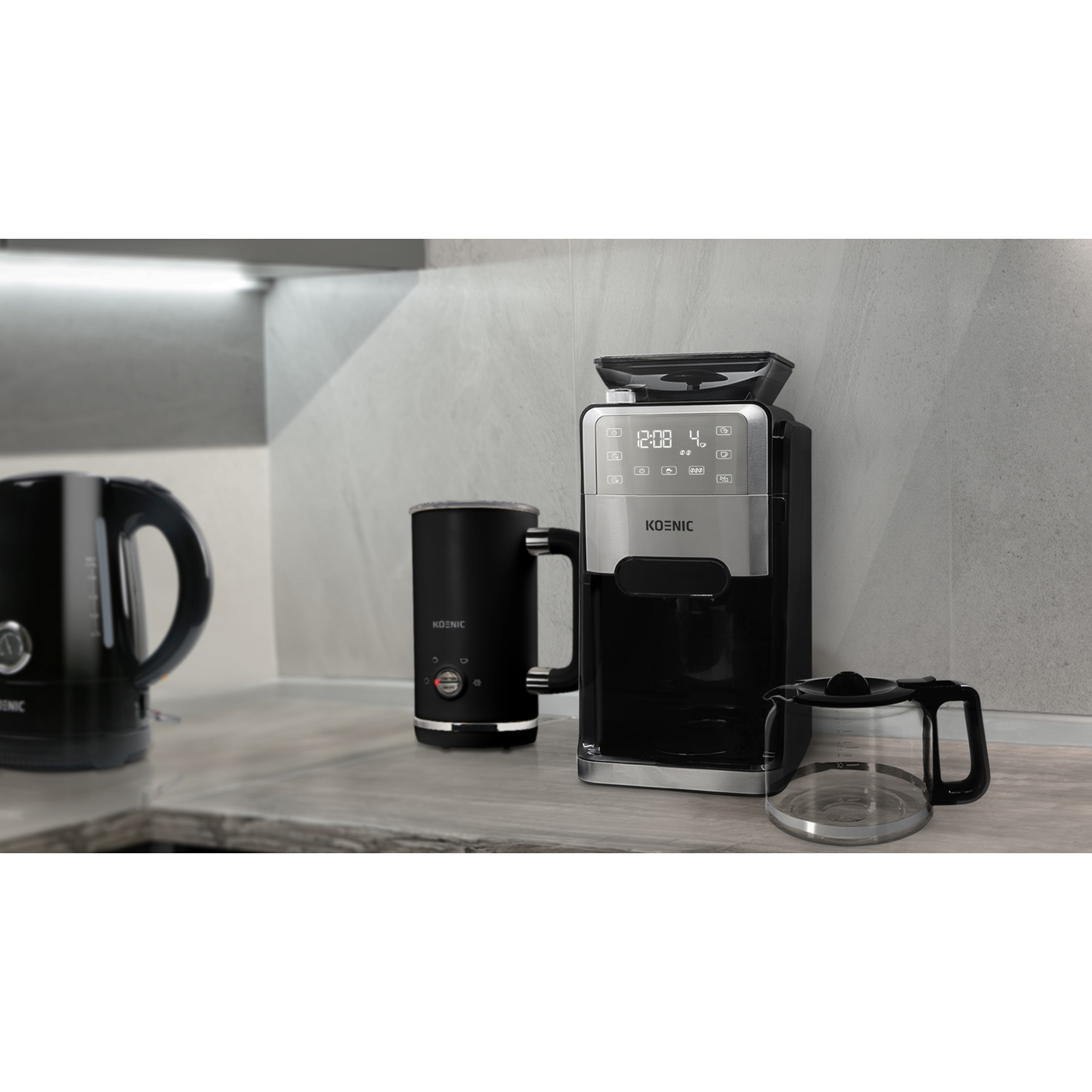 Una macchina per il caffè, un bollitore e uno schiumatore su un piano di lavoro. Tutti gli articoli sono neri e argento.