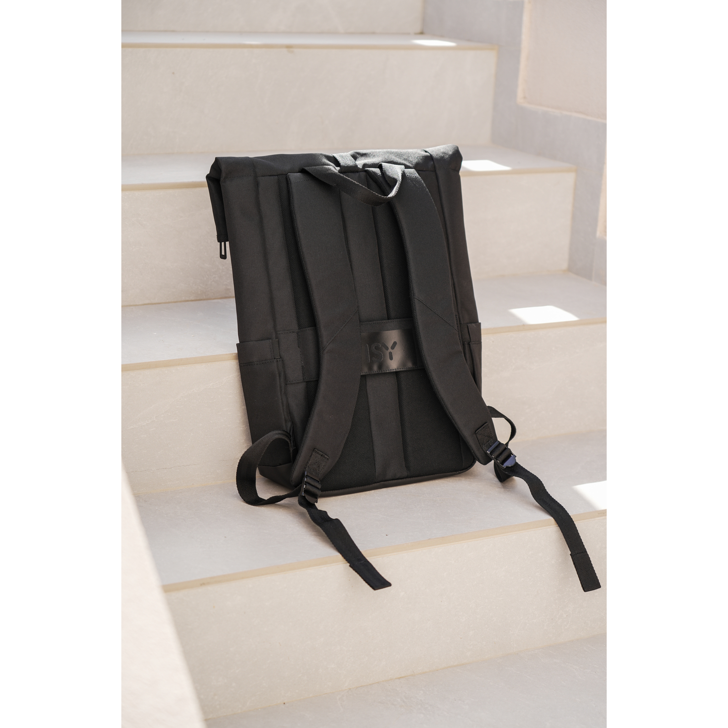 Sac à dos noir sur un escalier beige. Le sac à dos a des sangles et une poignée. Le fond est flou.
