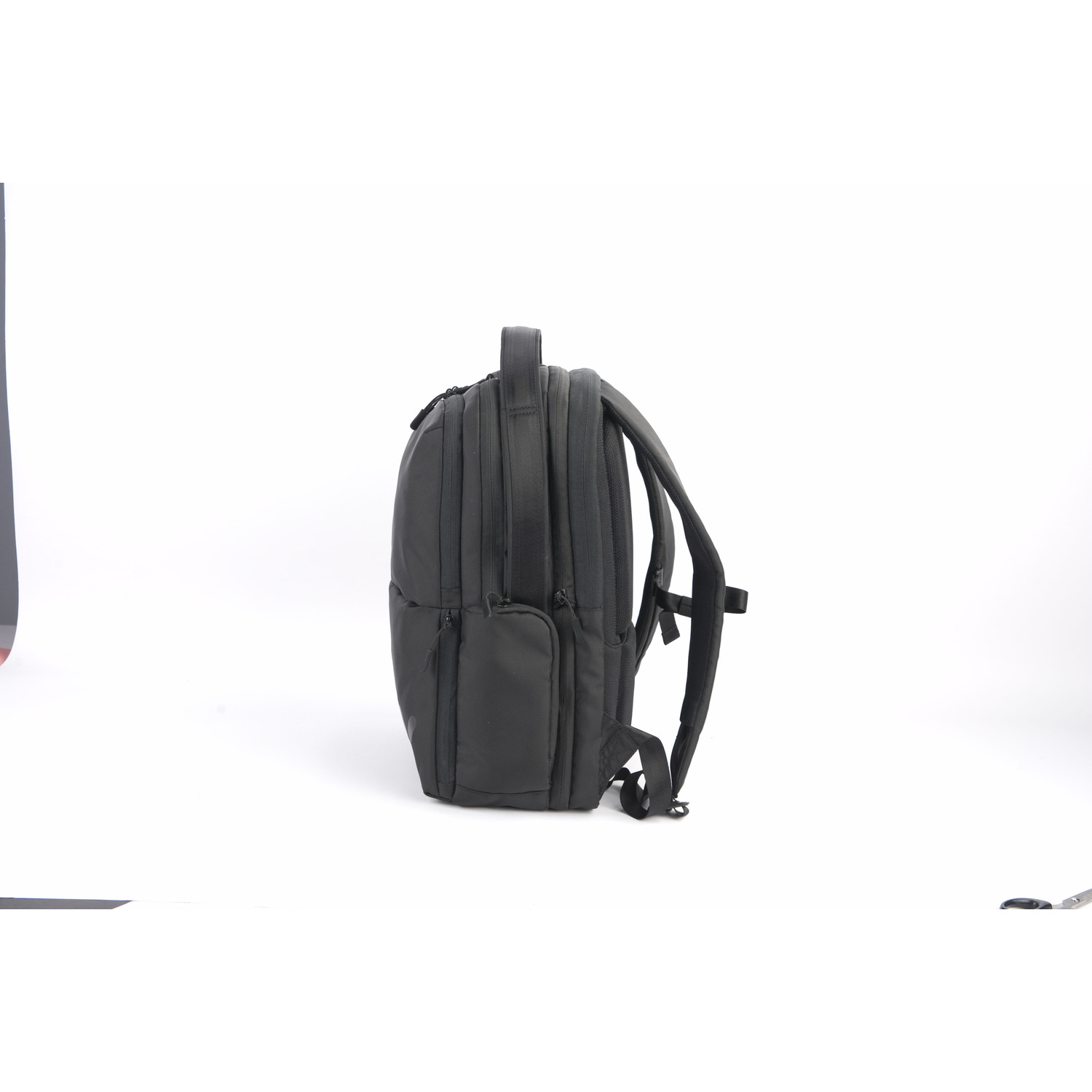 Sac à dos noir, vue latérale, fond blanc. A des poches et des sangles.