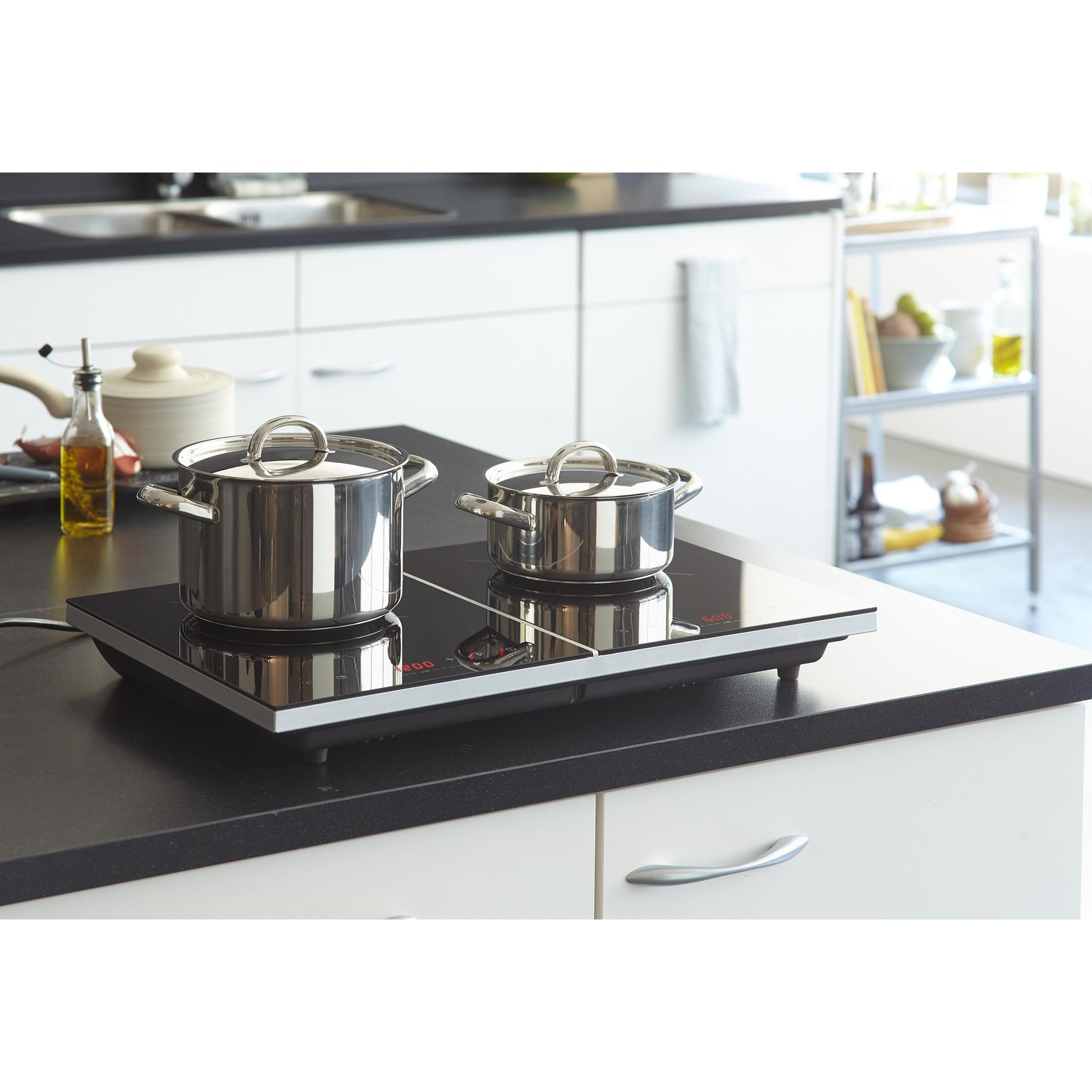 Twee roestvrijstalen potten op een zwarte inductiekookplaat. De setting is een moderne keuken.