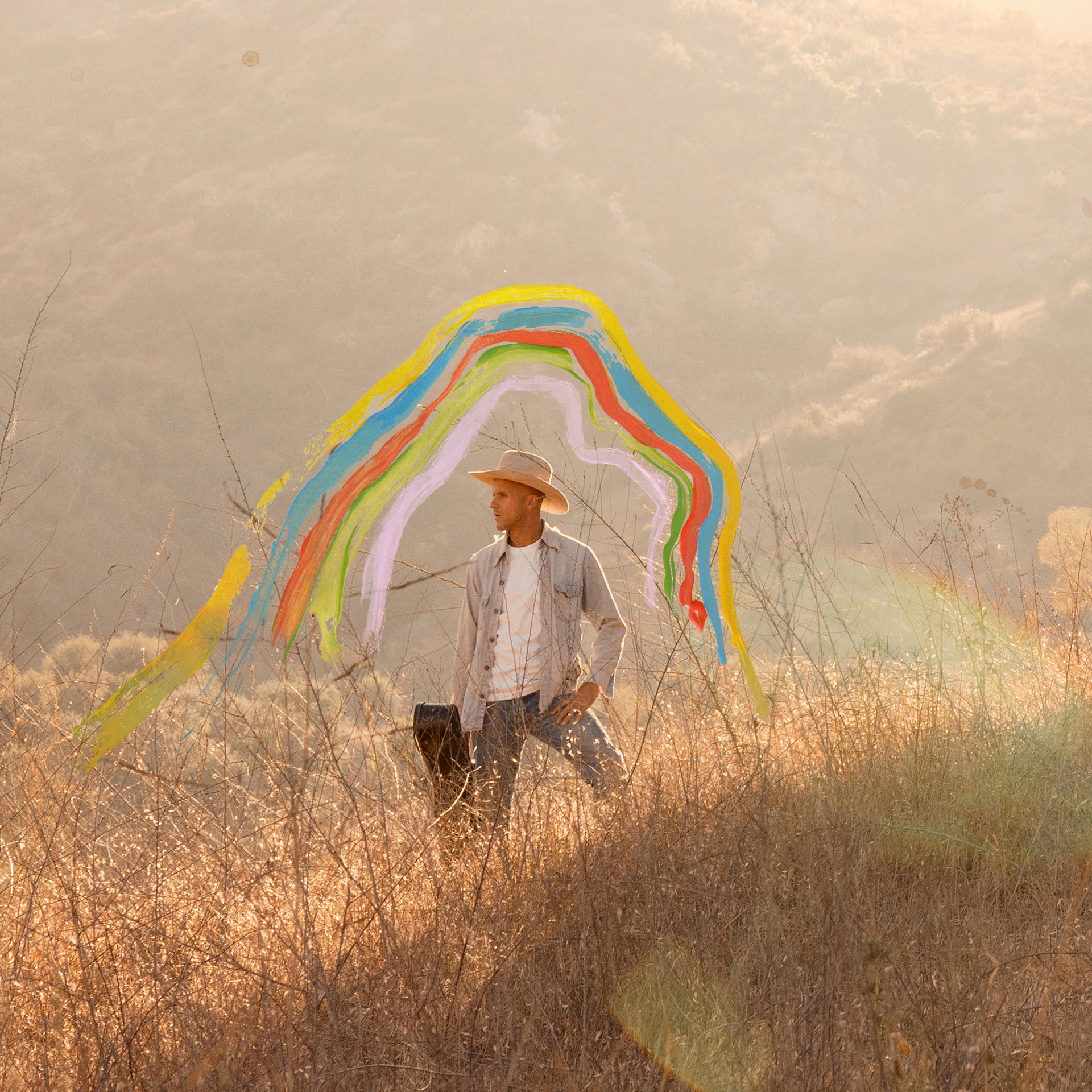 Een man met een hoed staat in een veld met een regenboog boven hem geschilderd.