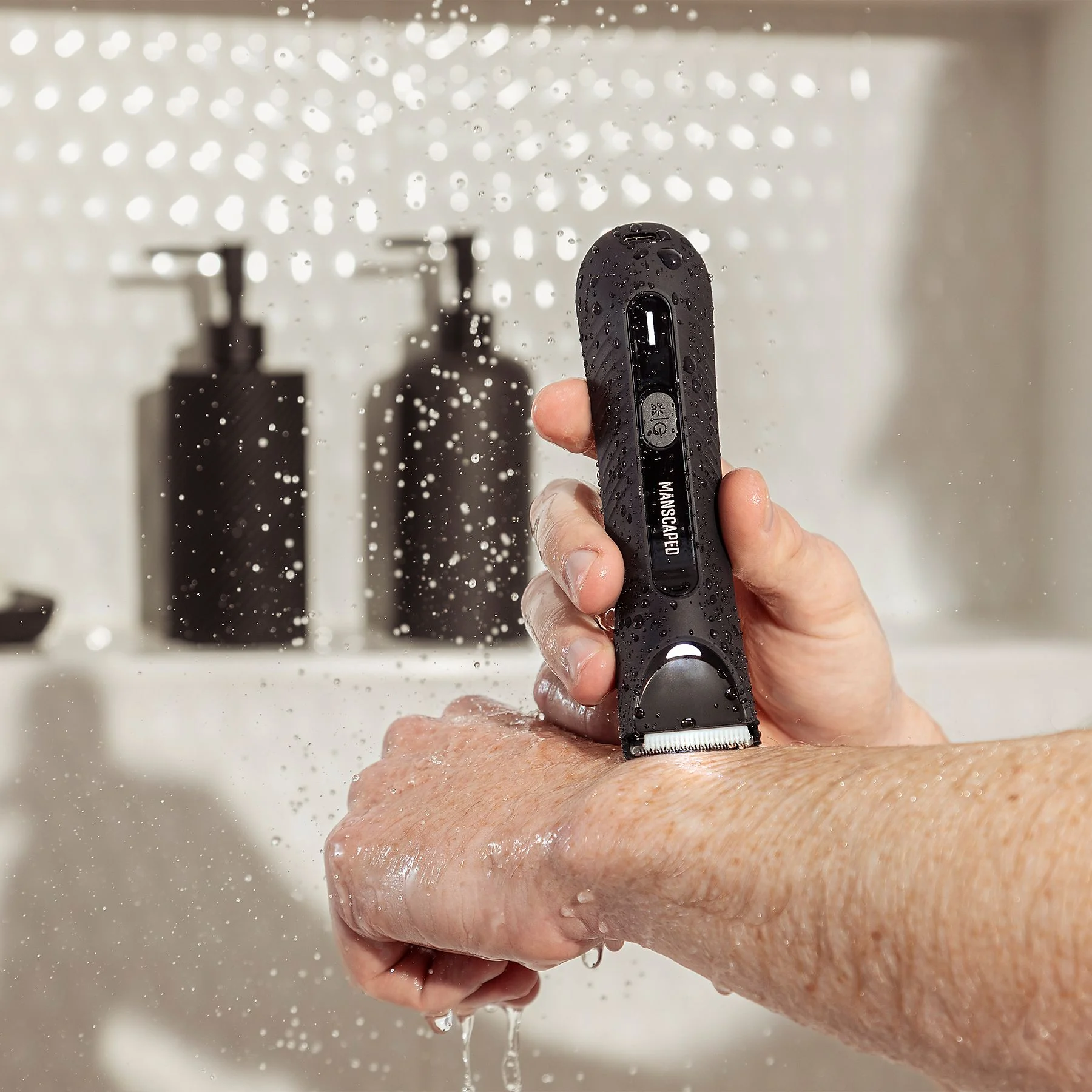 Mann rasiert Arm mit schwarzem Manscaped Trimmer unter der Dusche.