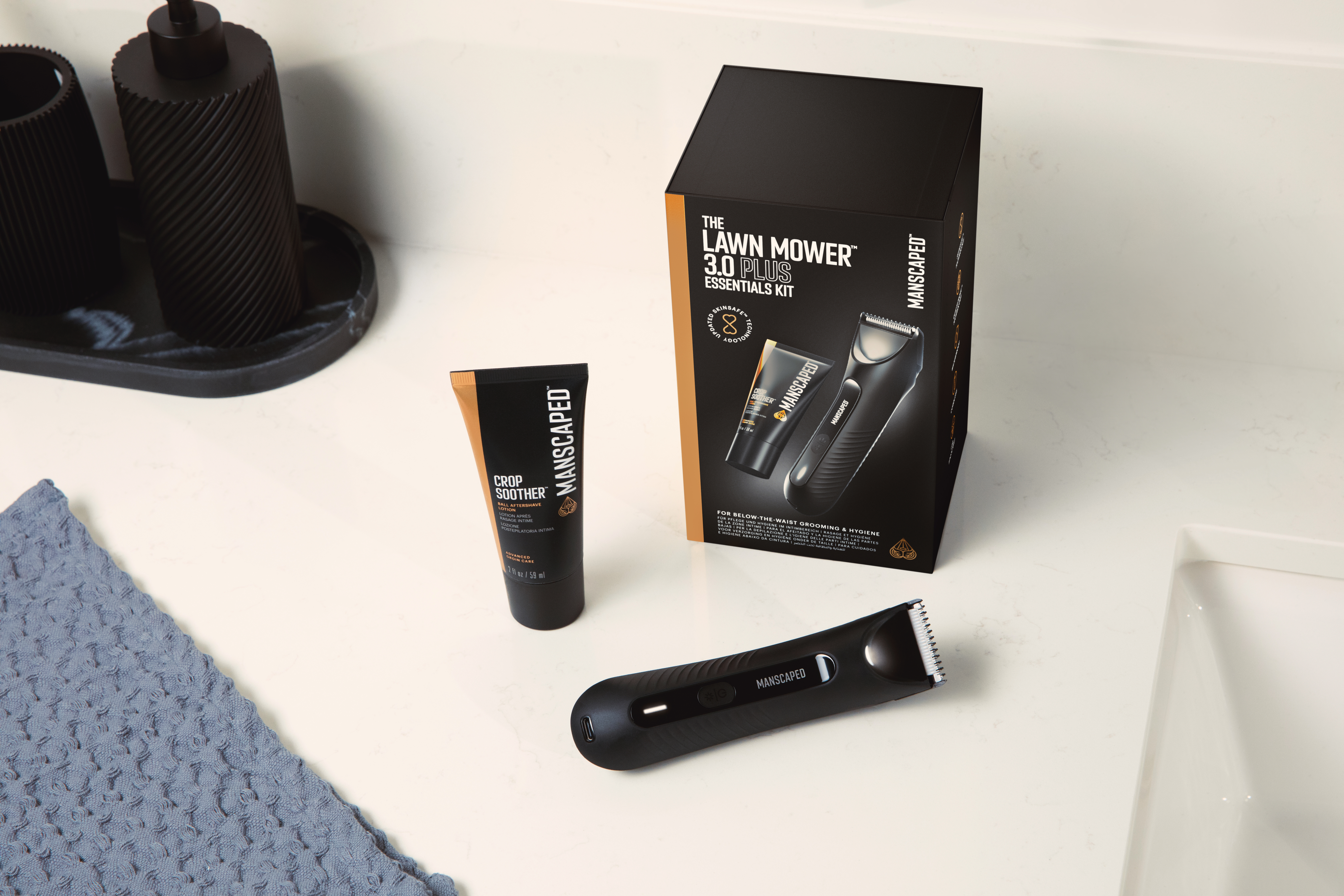 Eine schwarze Rasier-Set-Box, ein Trimmer und eine Tube Lotion liegen auf einer weißen Arbeitsplatte. Links liegt ein blaues Handtuch.