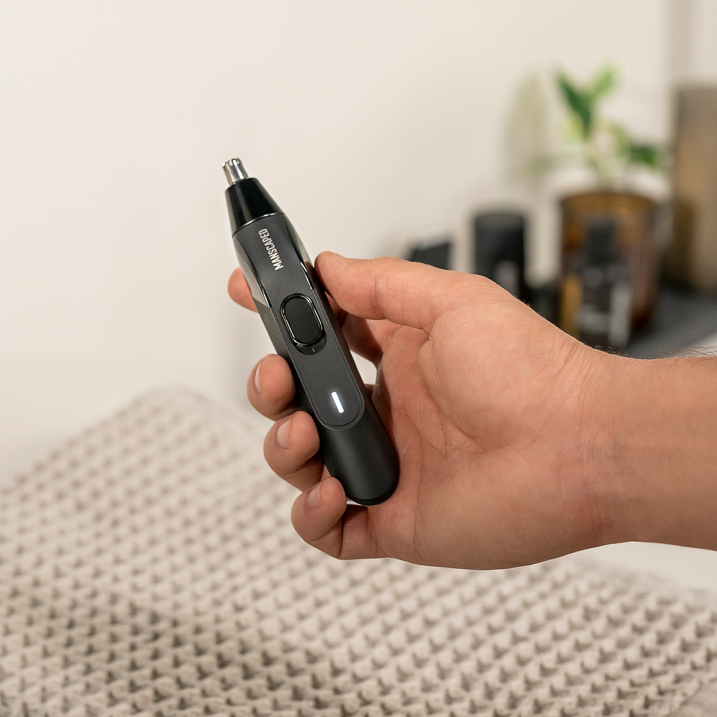 Person hält einen schwarzen Nasenhaartrimmer. Der Hintergrund hat eine weiße Wand.