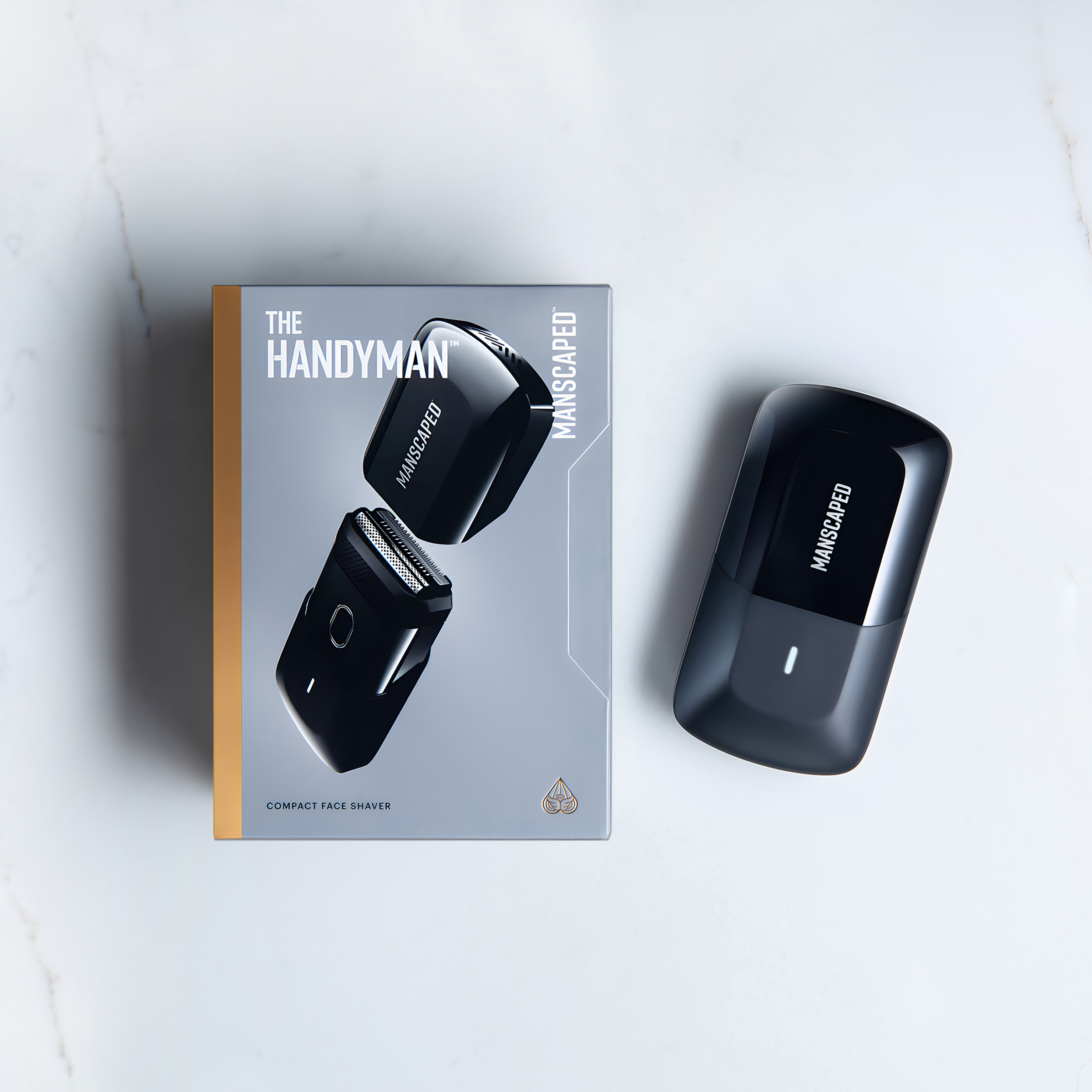Rasoir facial Manscaped noir et boîte sur marbre blanc. La boîte indique 'The Handyman' et 'Compact Face Shaver'.