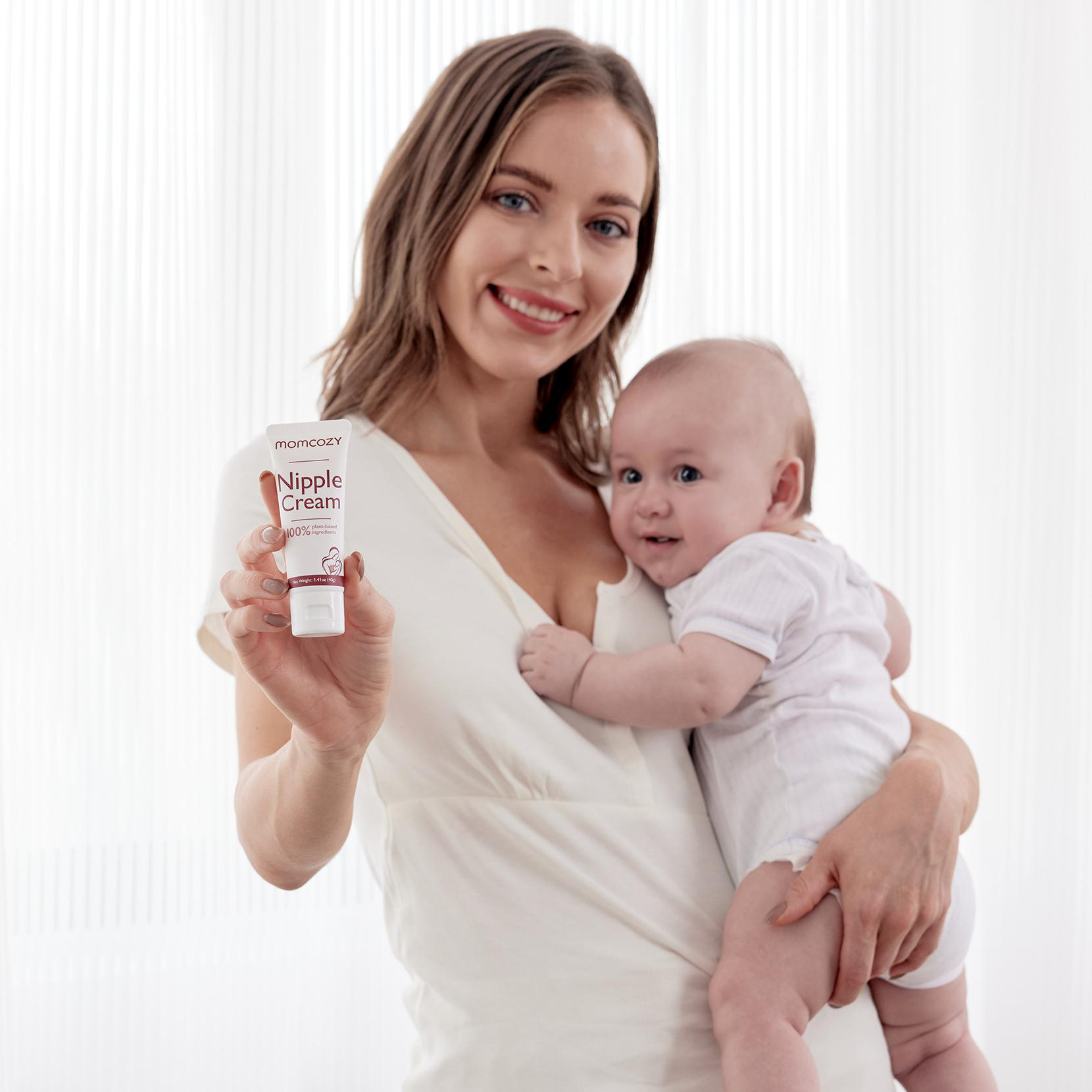 Eine Frau hält eine Brustwarzencreme-Tube, Baby auf dem Arm.