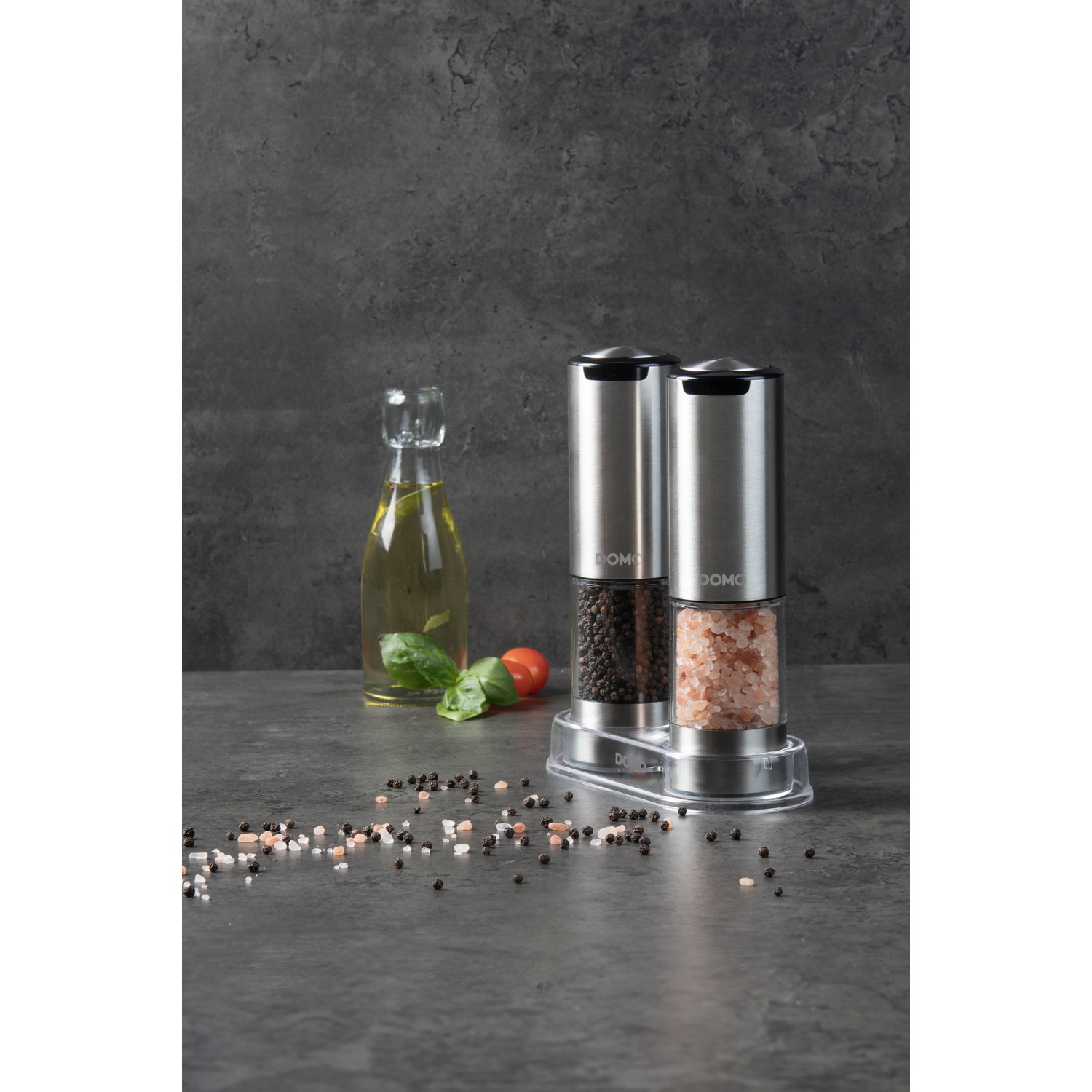 Two electric pepper grinders on a stand, with oil and spices on the table.