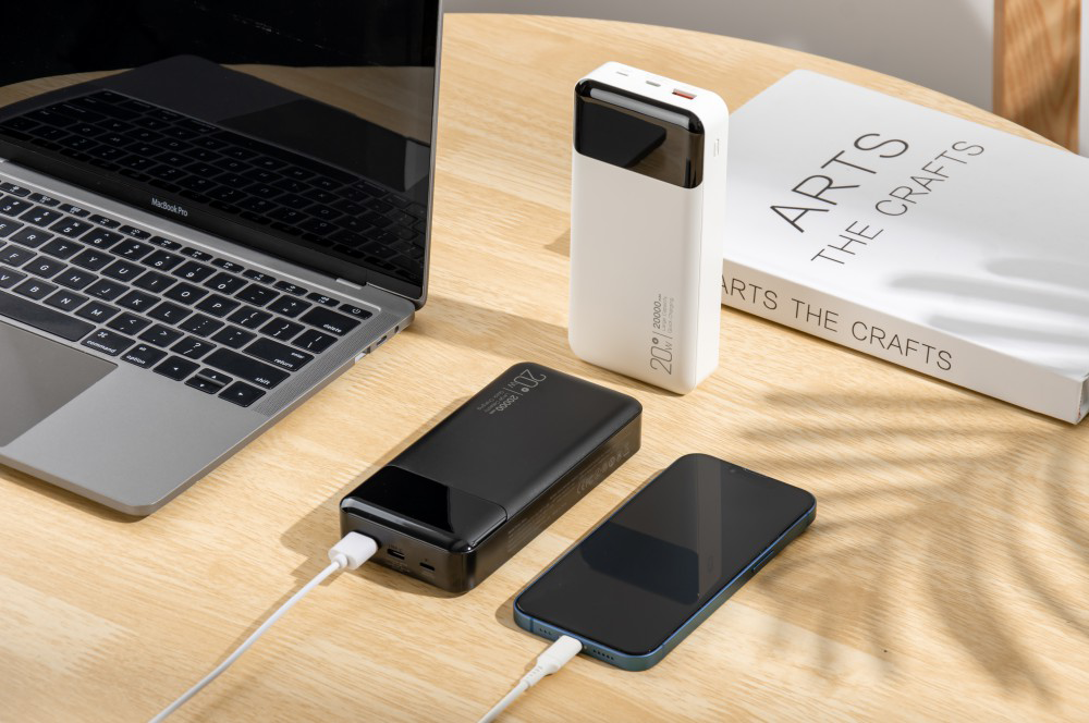 Egy laptop, egy fekete power bank, egy fehér power bank és egy okostelefon az asztalon.