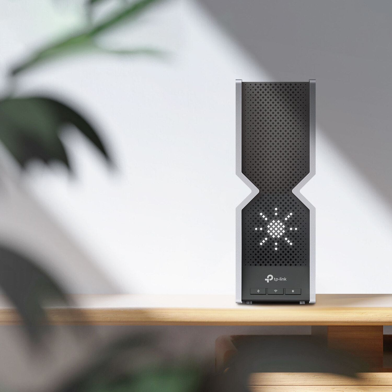 Un routeur TP-Link noir et argent sur une surface en bois contre un fond blanc avec une plante verte.
