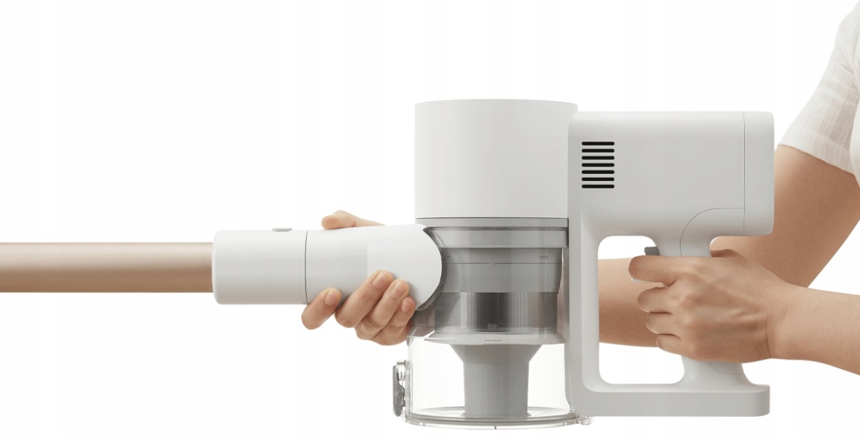 Ręka trzyma biały, bezprzewodowy odkurzacz ze złotą rurą przedłużającą, na białym tle.