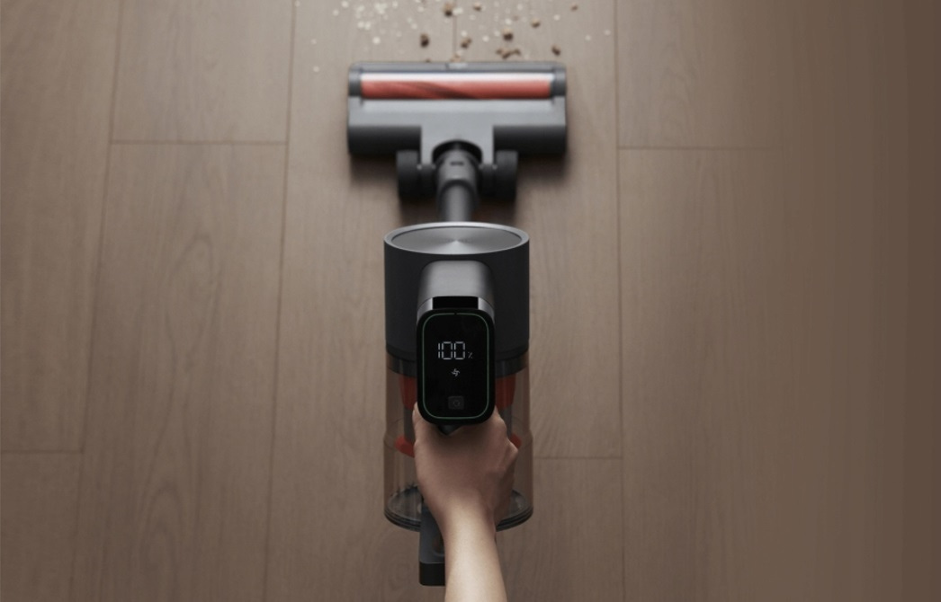 Ręka trzymająca odkurzacz, wyświetlacz cyfrowy pokazujący 100%.