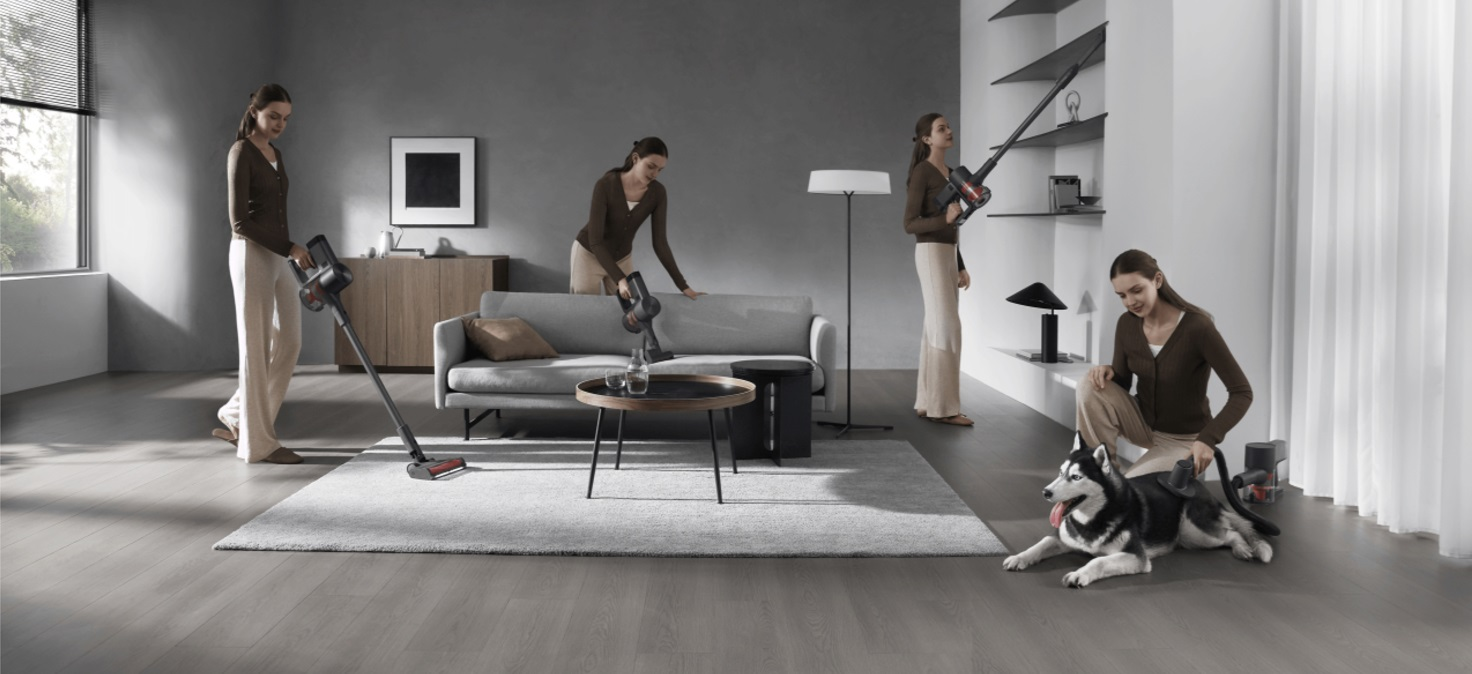 Kobieta odkurza. Używa odkurzacza na dywanie, sofie i innych powierzchniach. W pobliżu leży pies.