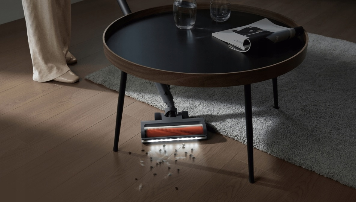 Odkurzacz czyszczący podłogę, z ciemnym stołem i rozrzuconymi w pobliżu śmieciami.