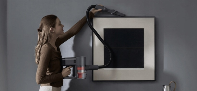 Kobieta odkurzająca obraz na ścianie odkurzaczem bezprzewodowym.