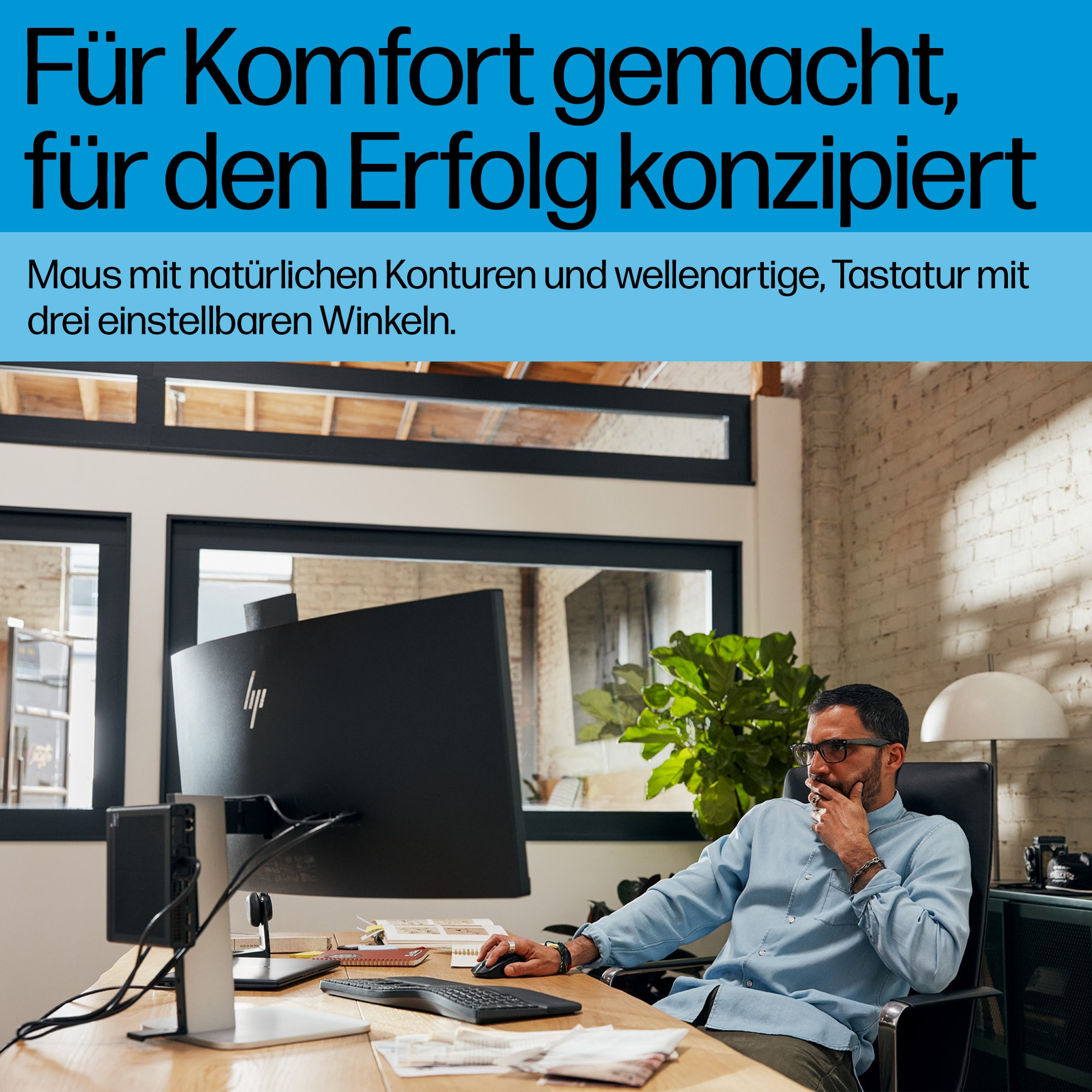 Mann im Büro mit schwarzer Tastatur und Maus. Schwarzer Monitor, Pflanze und Schreibtisch.