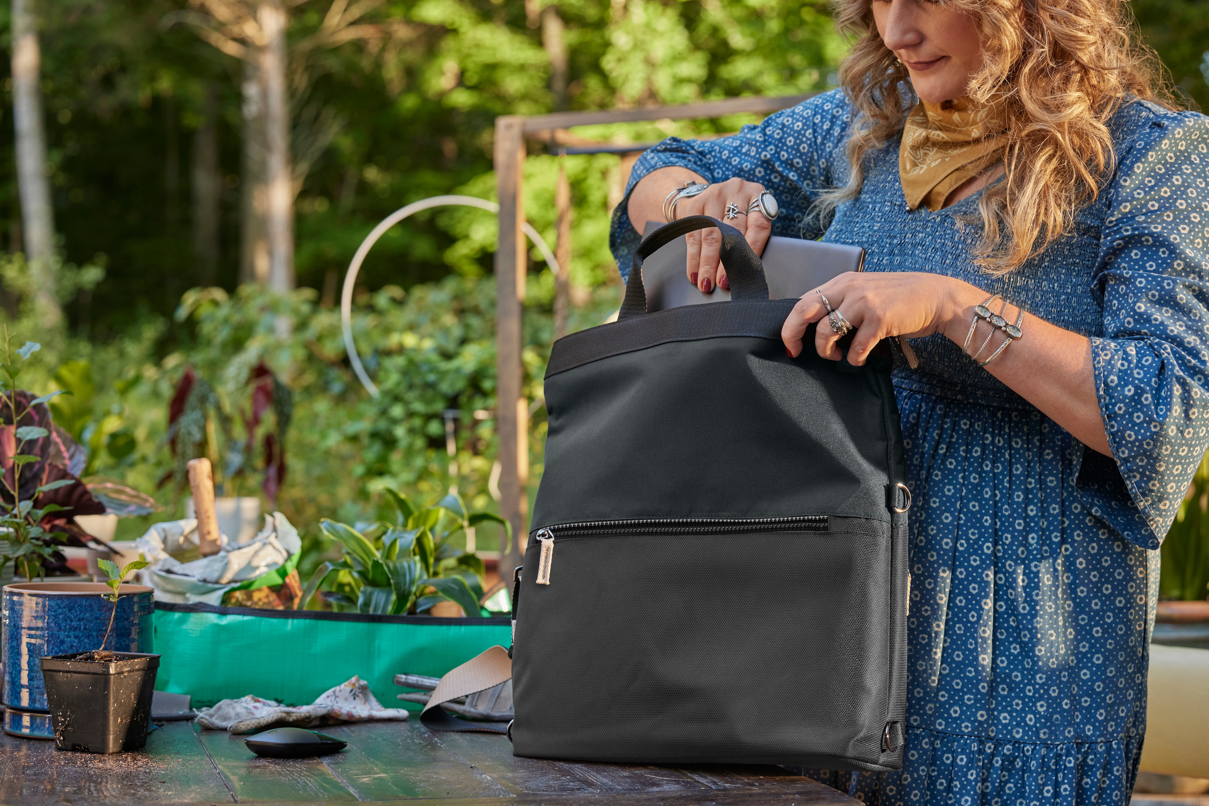 Femme dans jardin mettant ordinateur portable dans sac à dos noir. Plantes vertes.