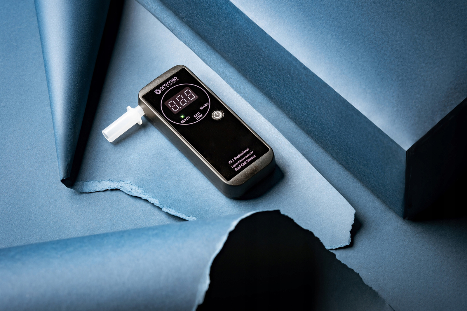 Czarny alkomat na niebieskim papierze. Wyświetla odczyt. Niebieskie tło.