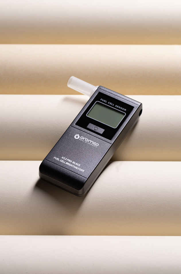 Czarny alkomat na beżowym tle. Posiada wyświetlacz cyfrowy i biały ustnik.