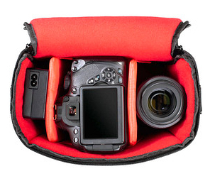 Otwarta torba na aparat, ukazująca aparat, obiektyw i akumulator, wszystko w czerwonym wnętrzu.
