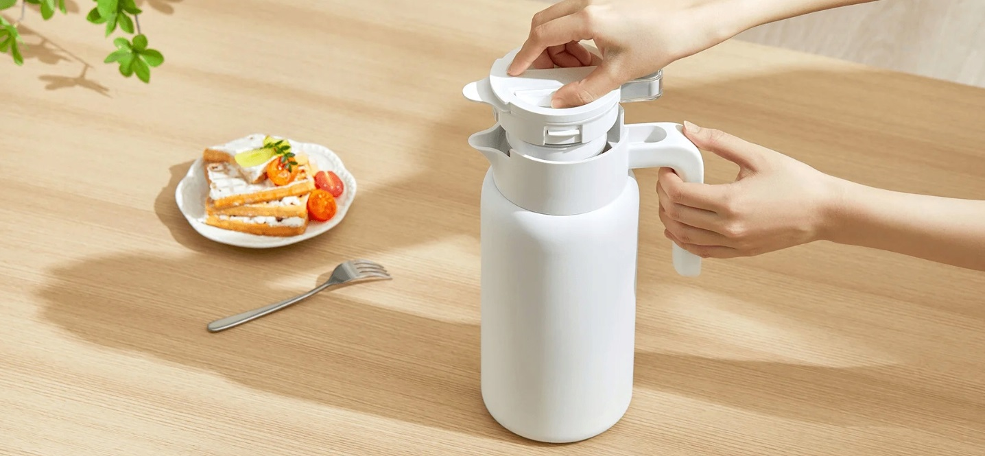 Biały termos przygotowywany, ręka operuje pokrywką.