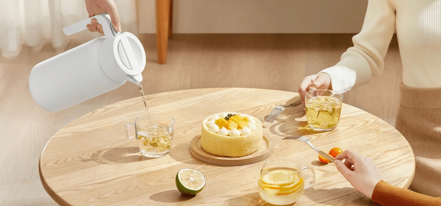 Osoba nalewa wodę do szklanki, ciasto i ludzie przy stole.