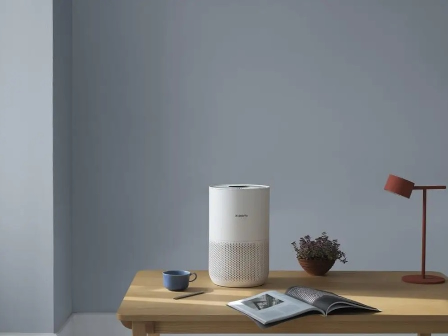 Biały oczyszczacz powietrza na drewnianym biurku z filiżanką, długopisem i rośliną.