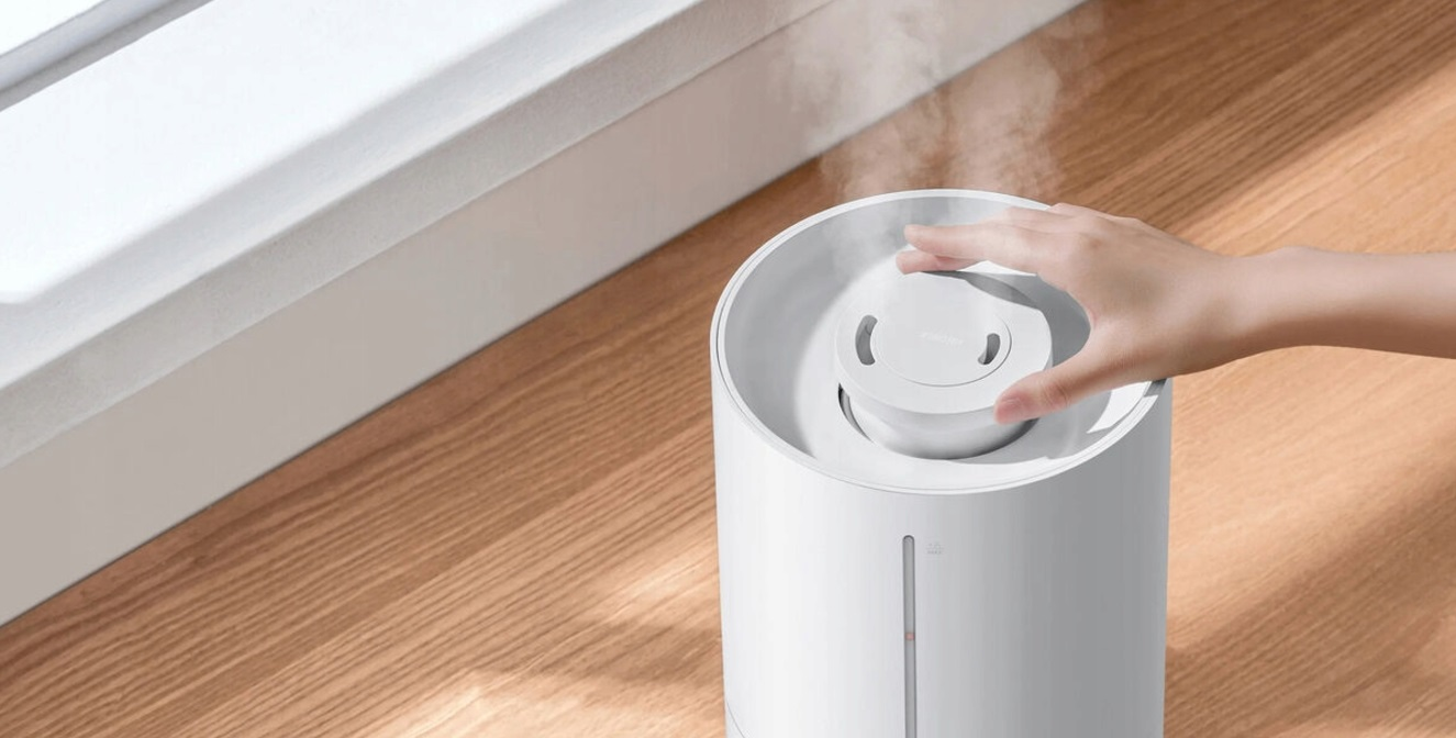 Biały nawilżacz powietrza z dłonią unoszącą się nad pokrywą, para wodna w górę.