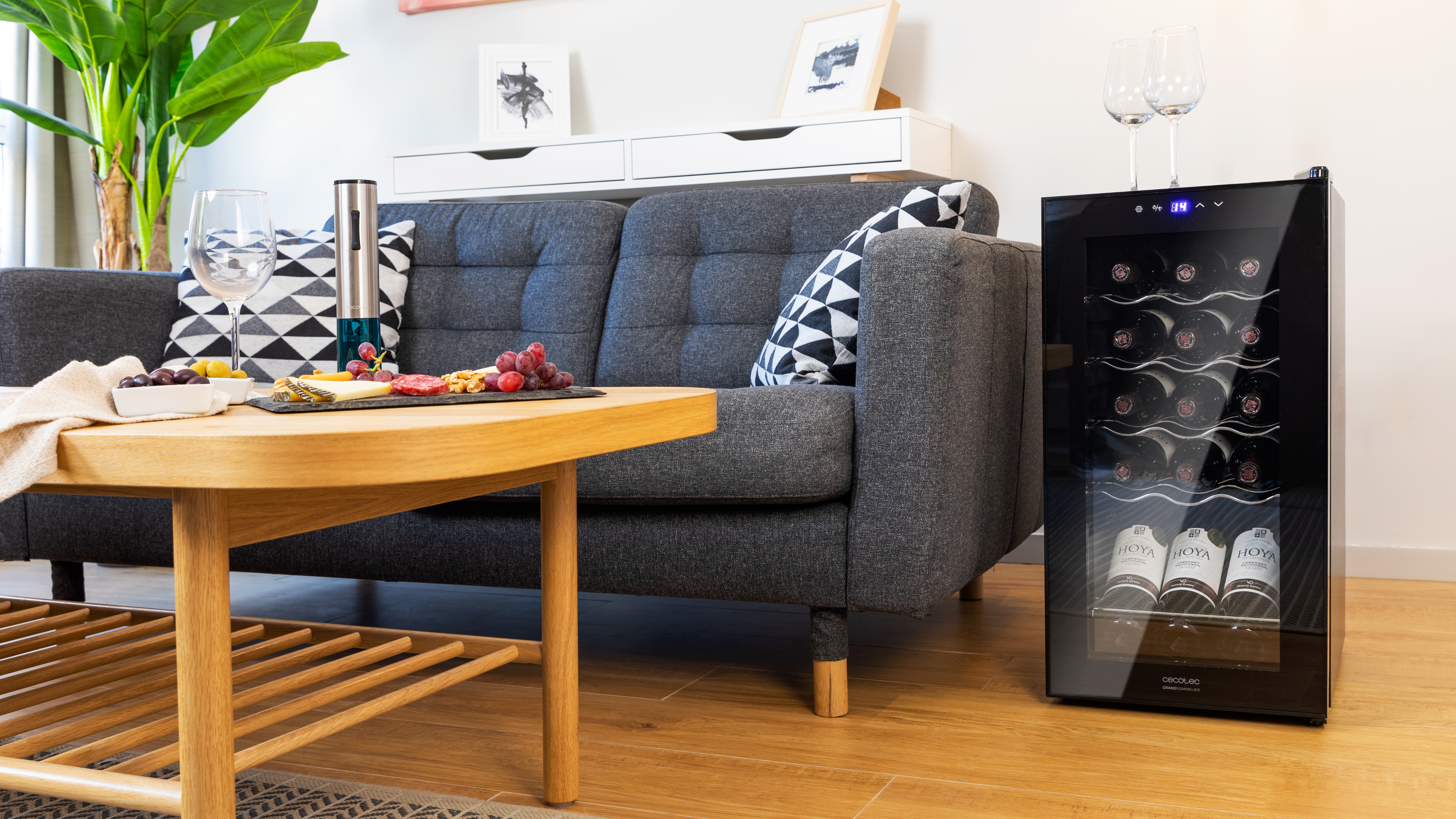 Salón con sofá gris, vinoteca y mesa con aperitivos.