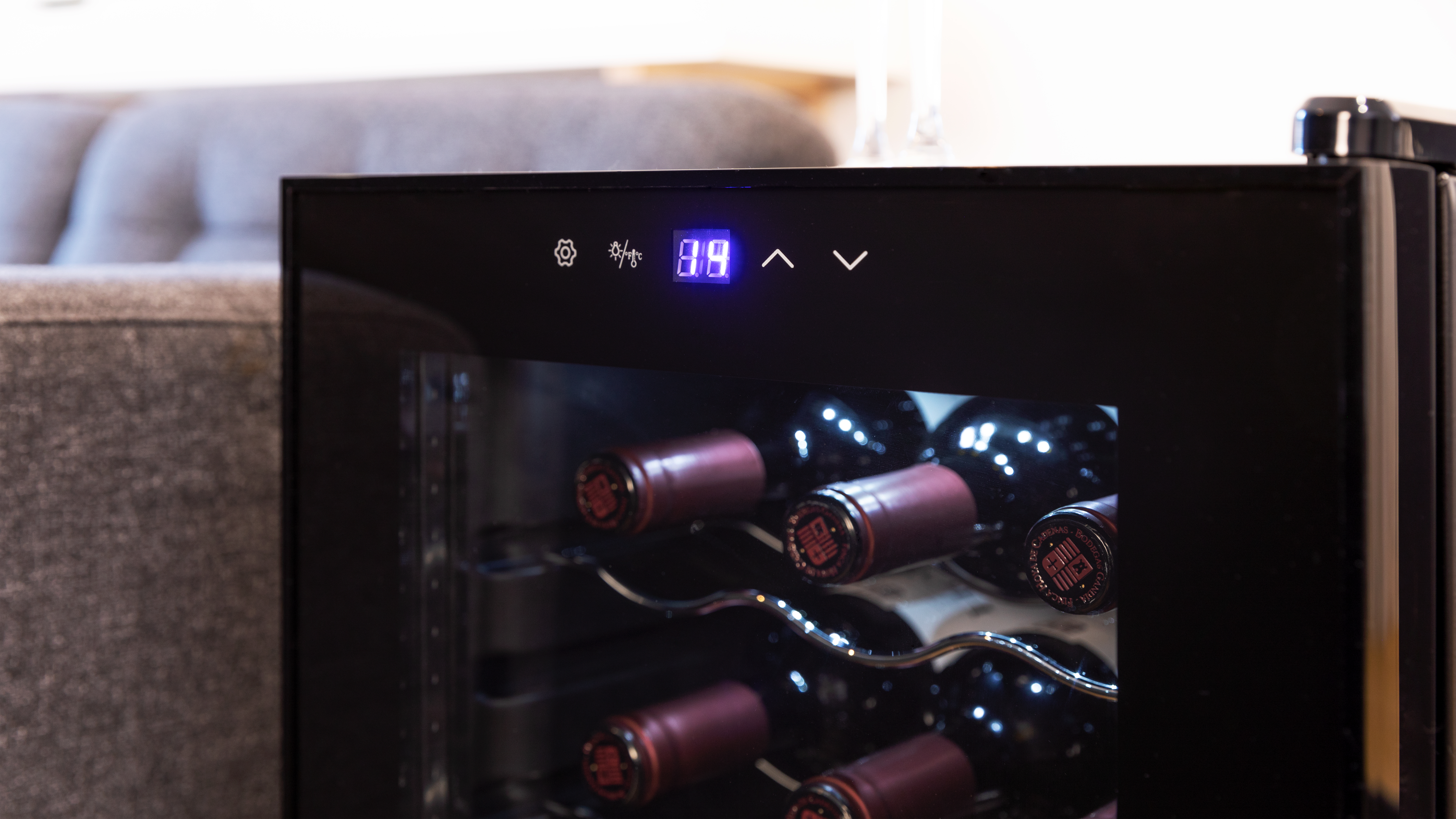 Enfriador de vino negro con botellas dentro, pantalla digital visible.