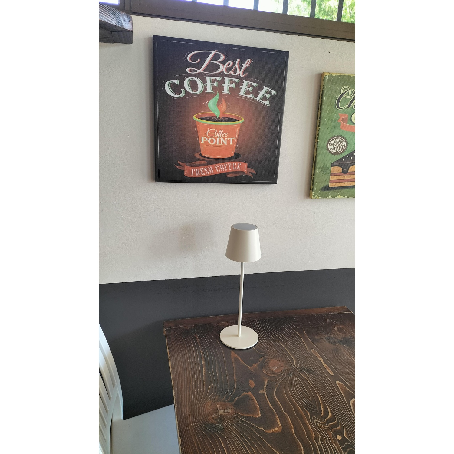 Un tavolo con una lampada e arte murale. Una lampada bianca sul tavolo e arte a tema caffè sulla parete.