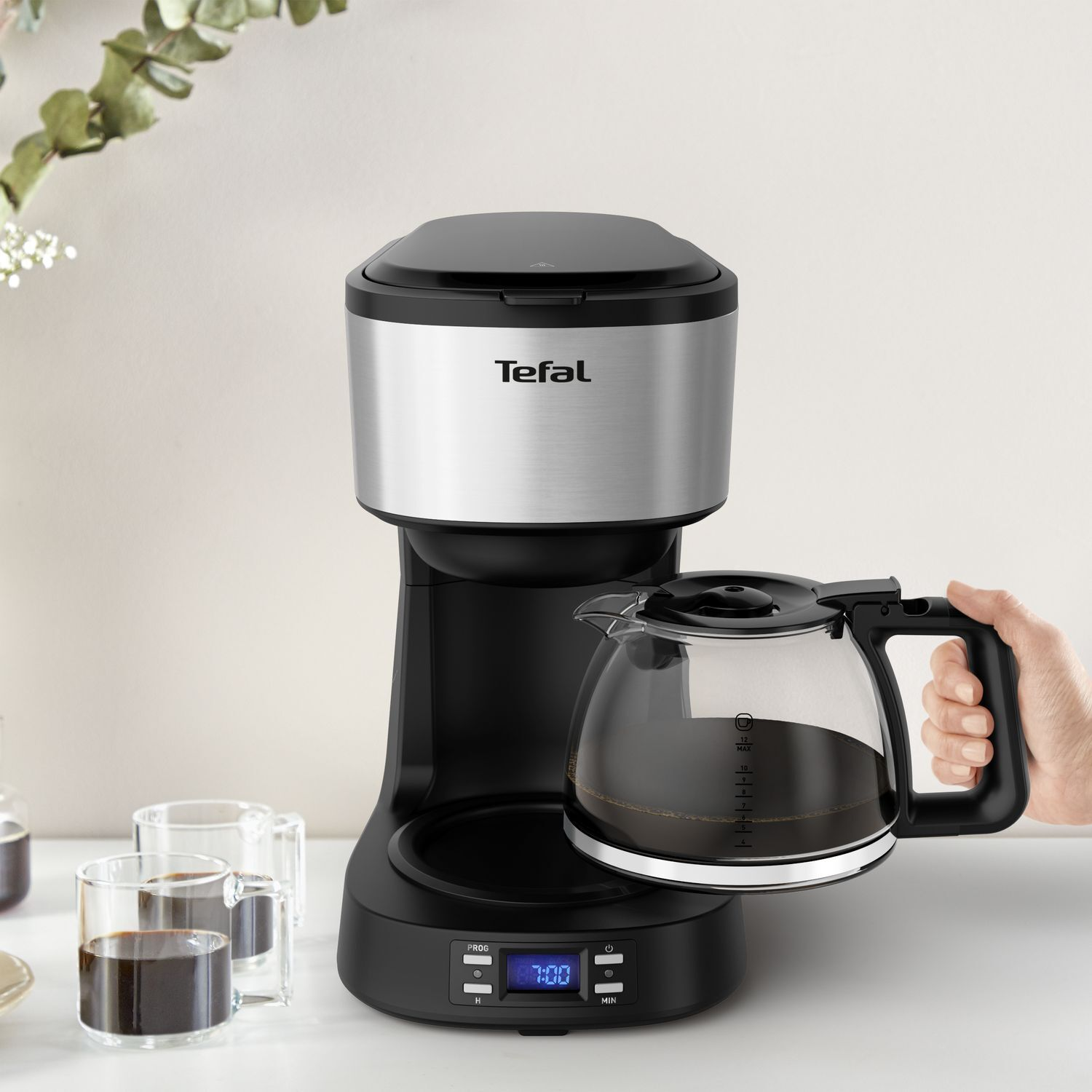 Black and silver Tefal coffee maker with glass carafe being held.
