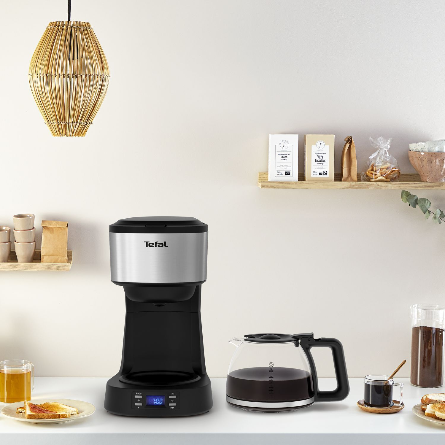 Coffee maker with a black body and silver top, glass carafe with coffee, and side table with breakfast.