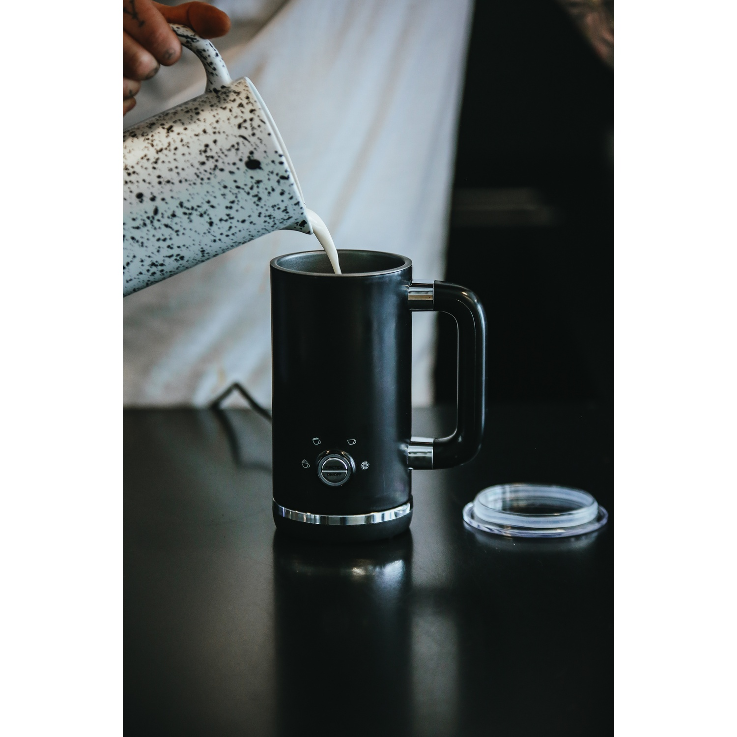 Una persona versa il latte in una tazza nera. La tazza ha un manico e un bordo argentato.