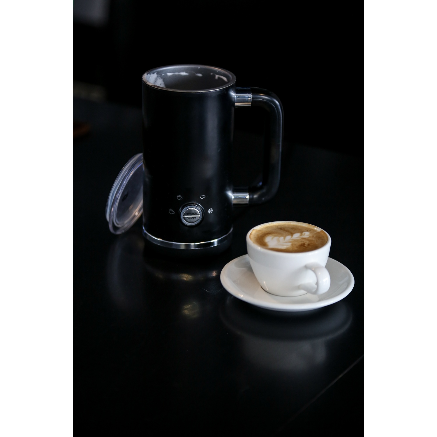 Caffettiera nera con cappuccino su un piattino bianco su una superficie nera.