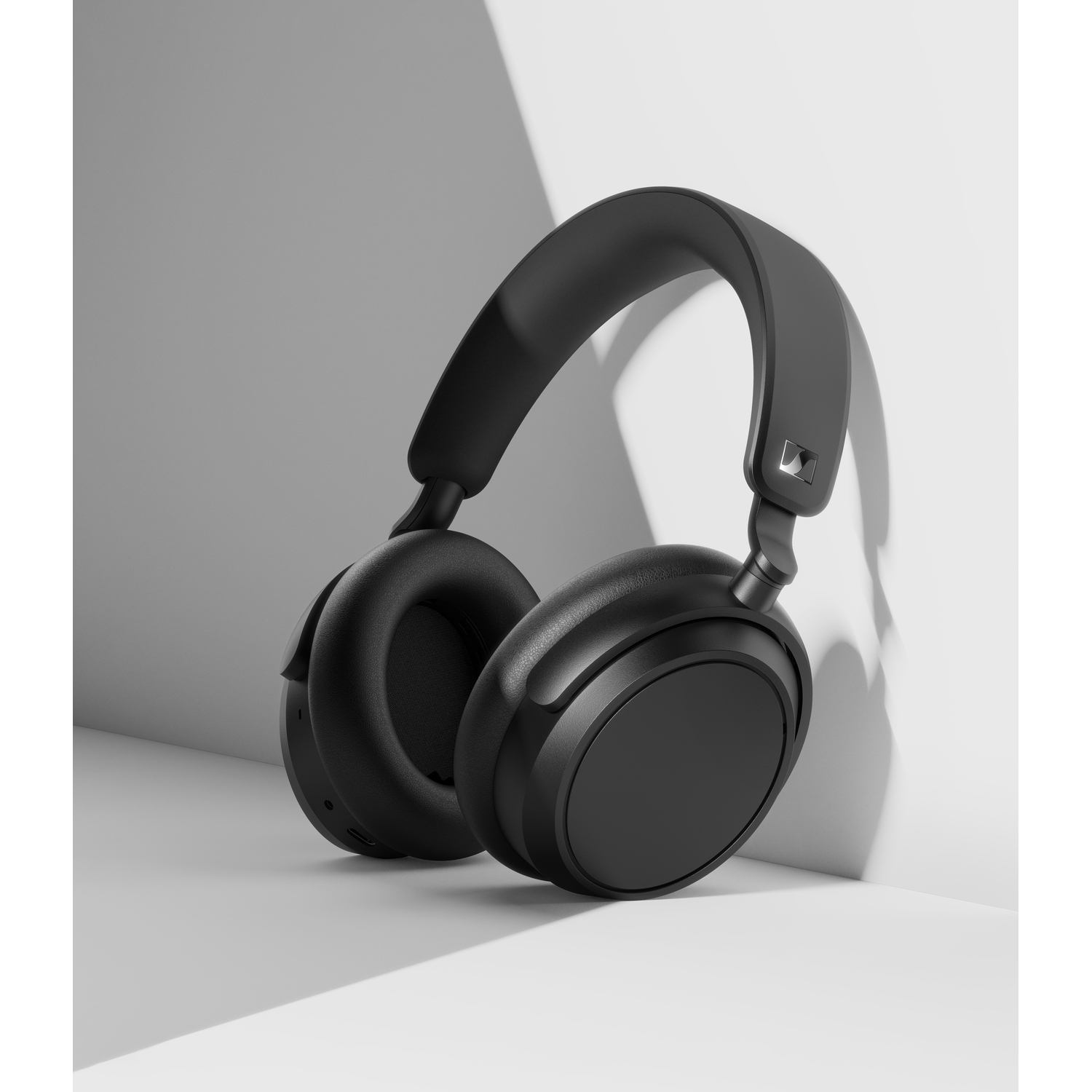 Black headphones resting on a white surface, grey background.
