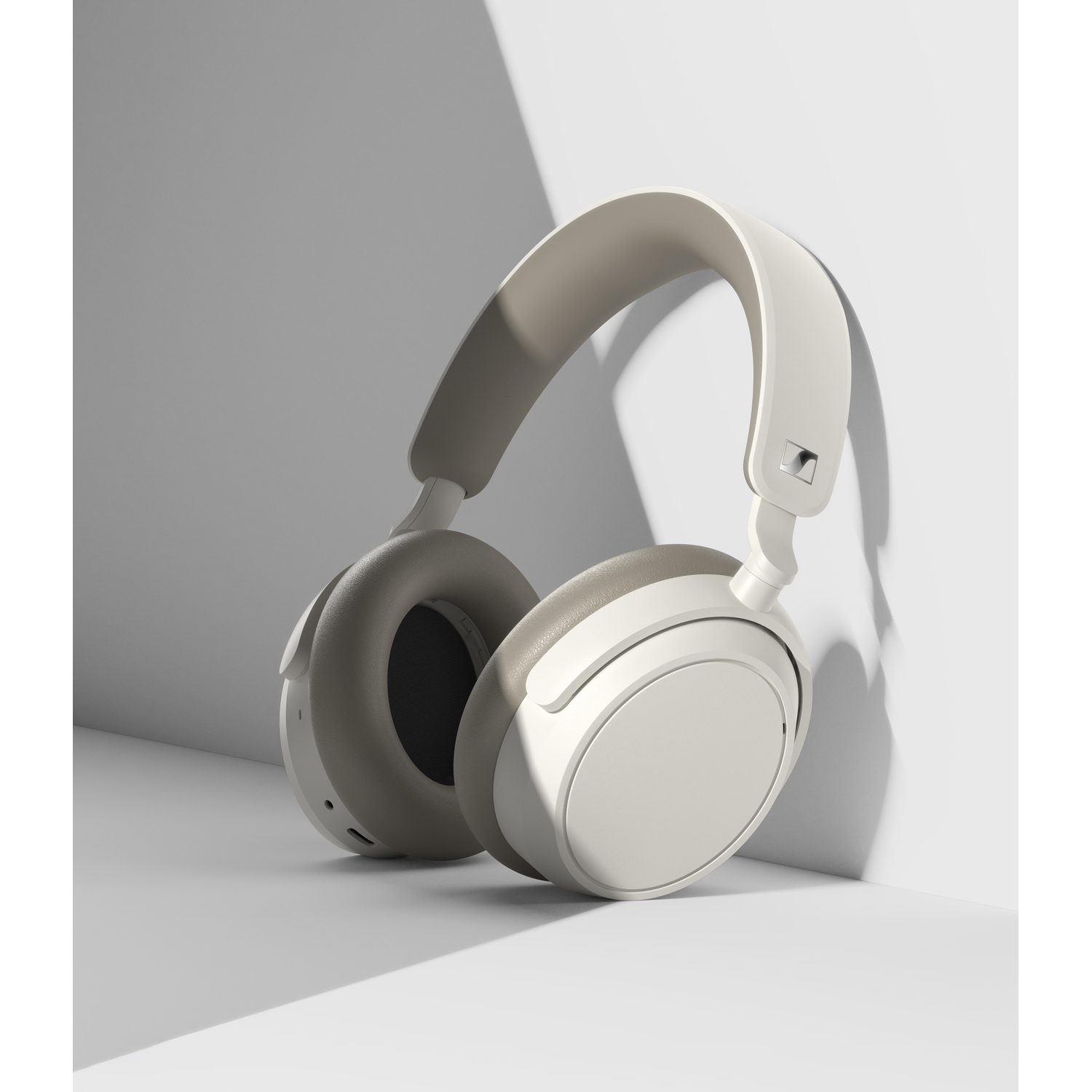 Casque audio blanc cassé avec bandeau et oreillettes gris clair. Repose sur une surface blanche et grise.