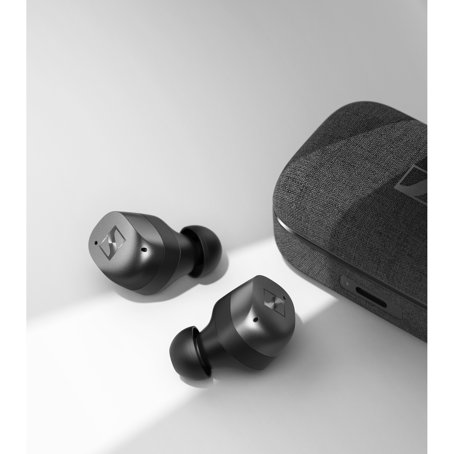 Two black wireless earbuds and their charging case, all on a white surface.