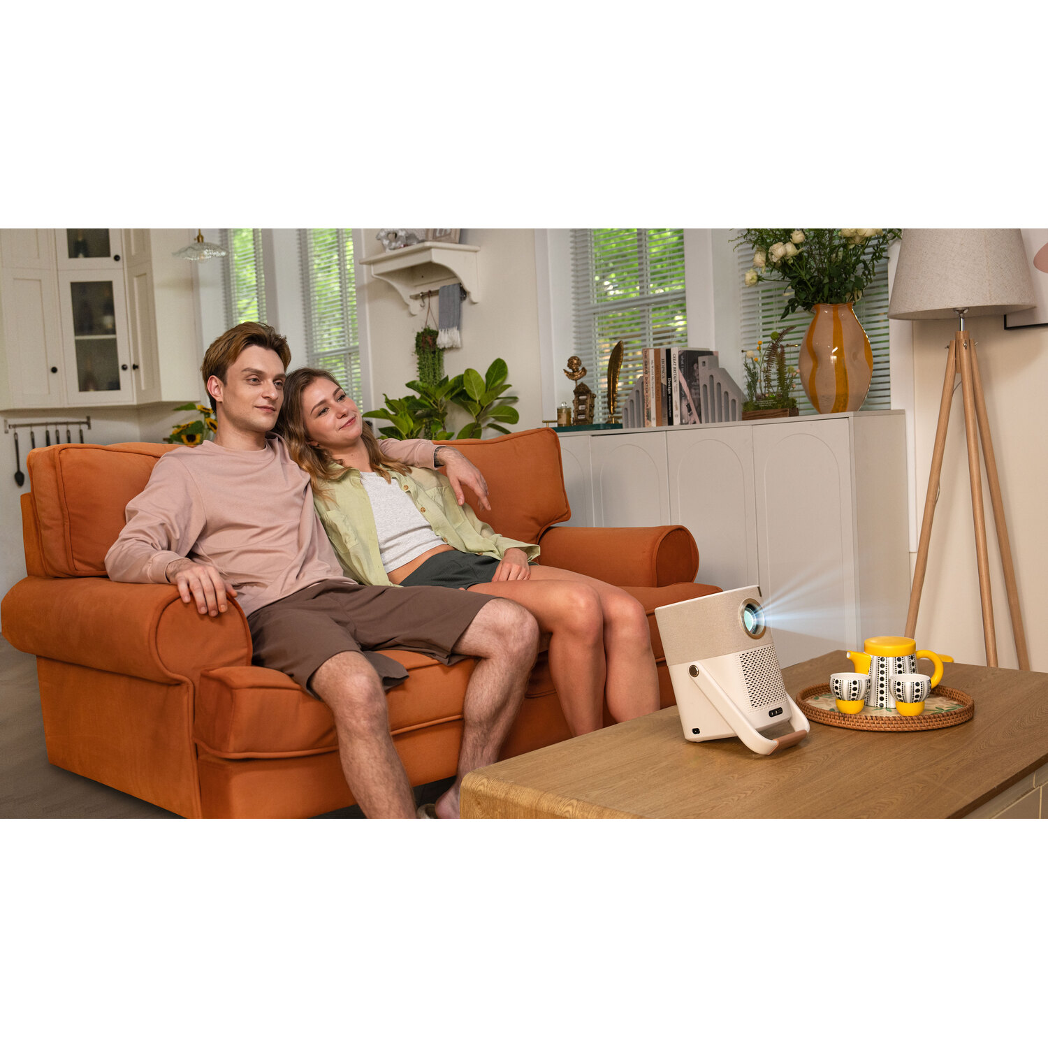 Couple sur canapé orange regardant un écran de projecteur, tasse jaune sur table.