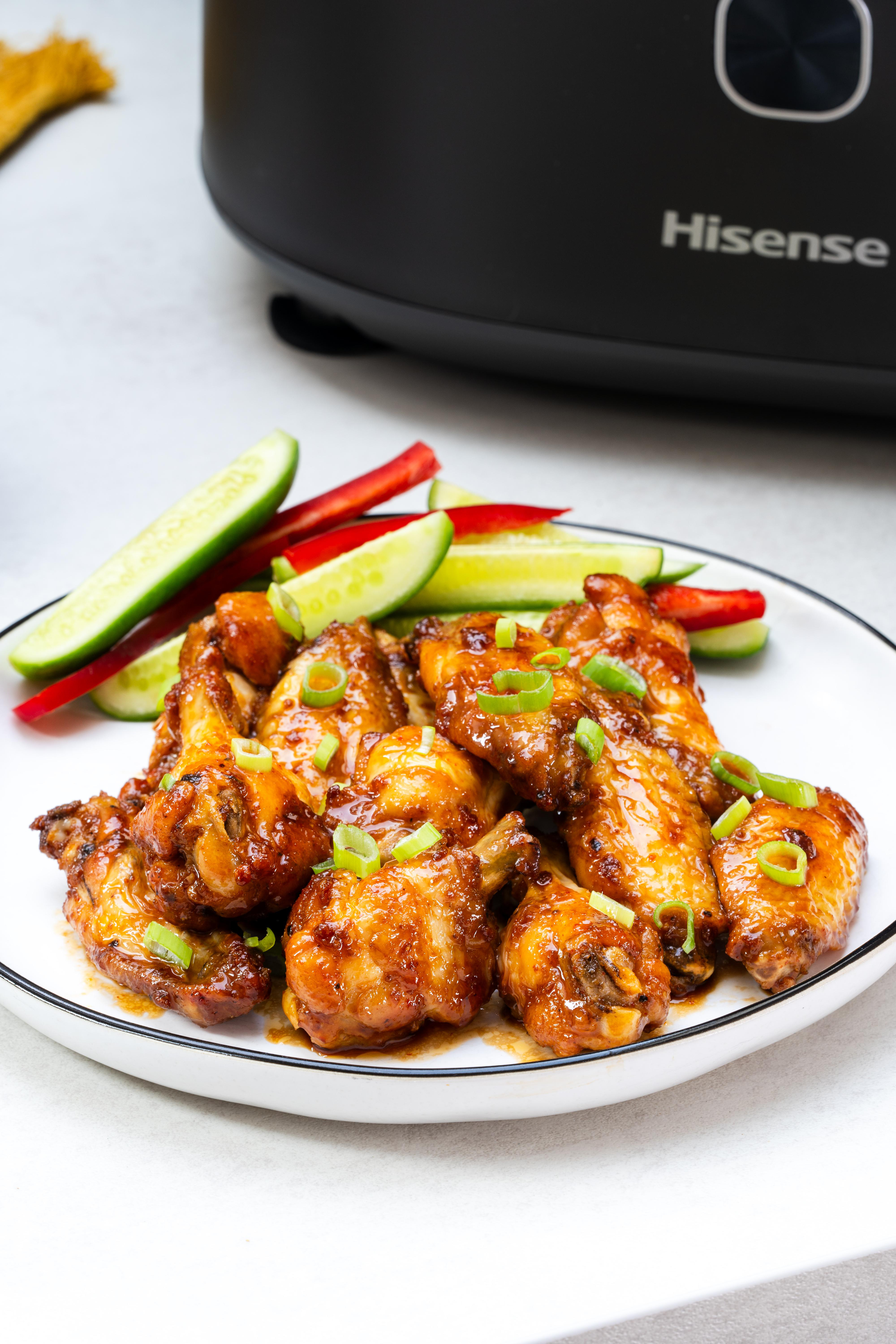 Teller mit Chicken Wings, Gurken- und Paprikascheiben, im Hintergrund ein Slow Cooker.